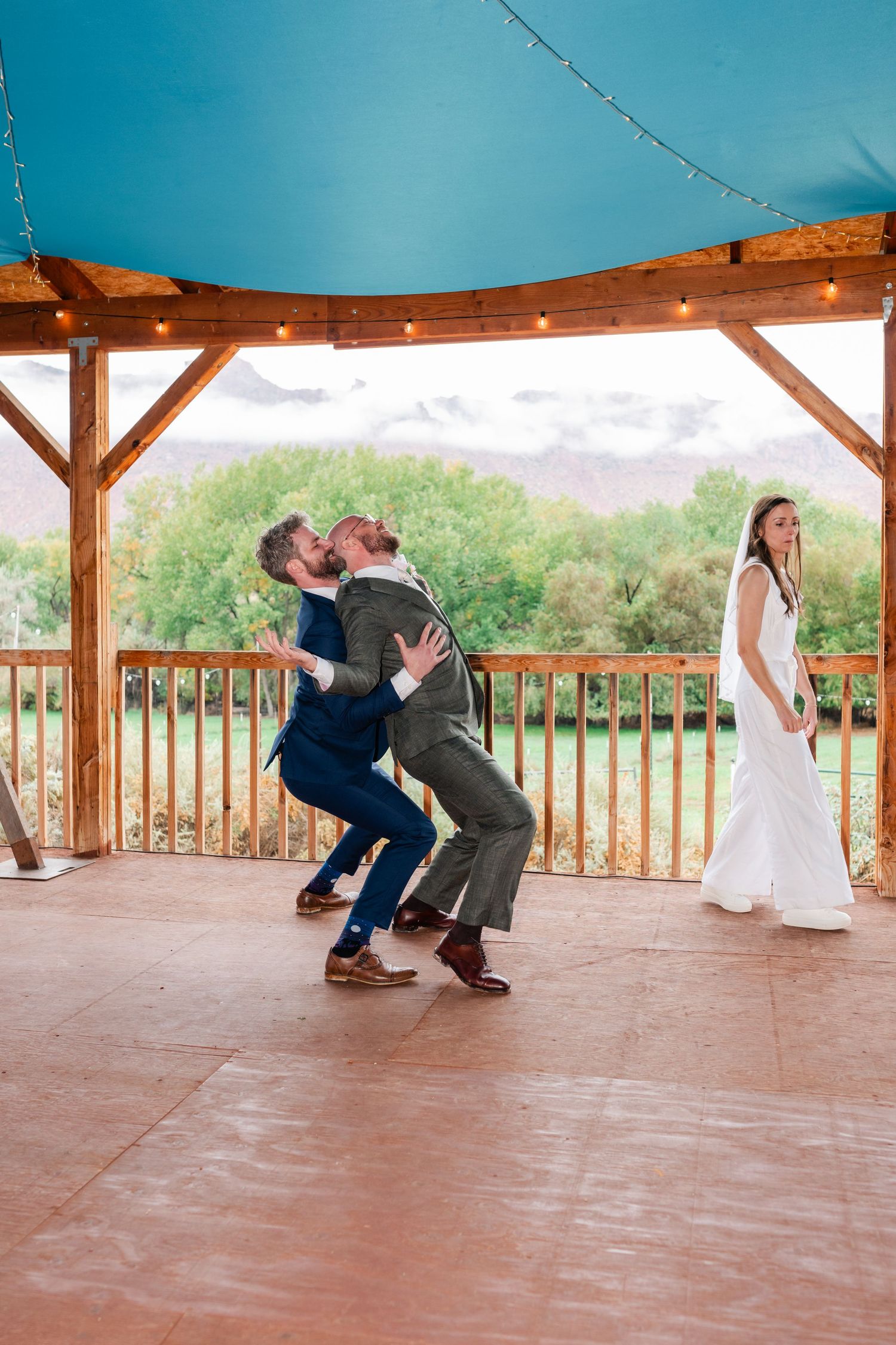 Playful dance dip sequence captured in outdoor pavilion with blue sky backdrop.