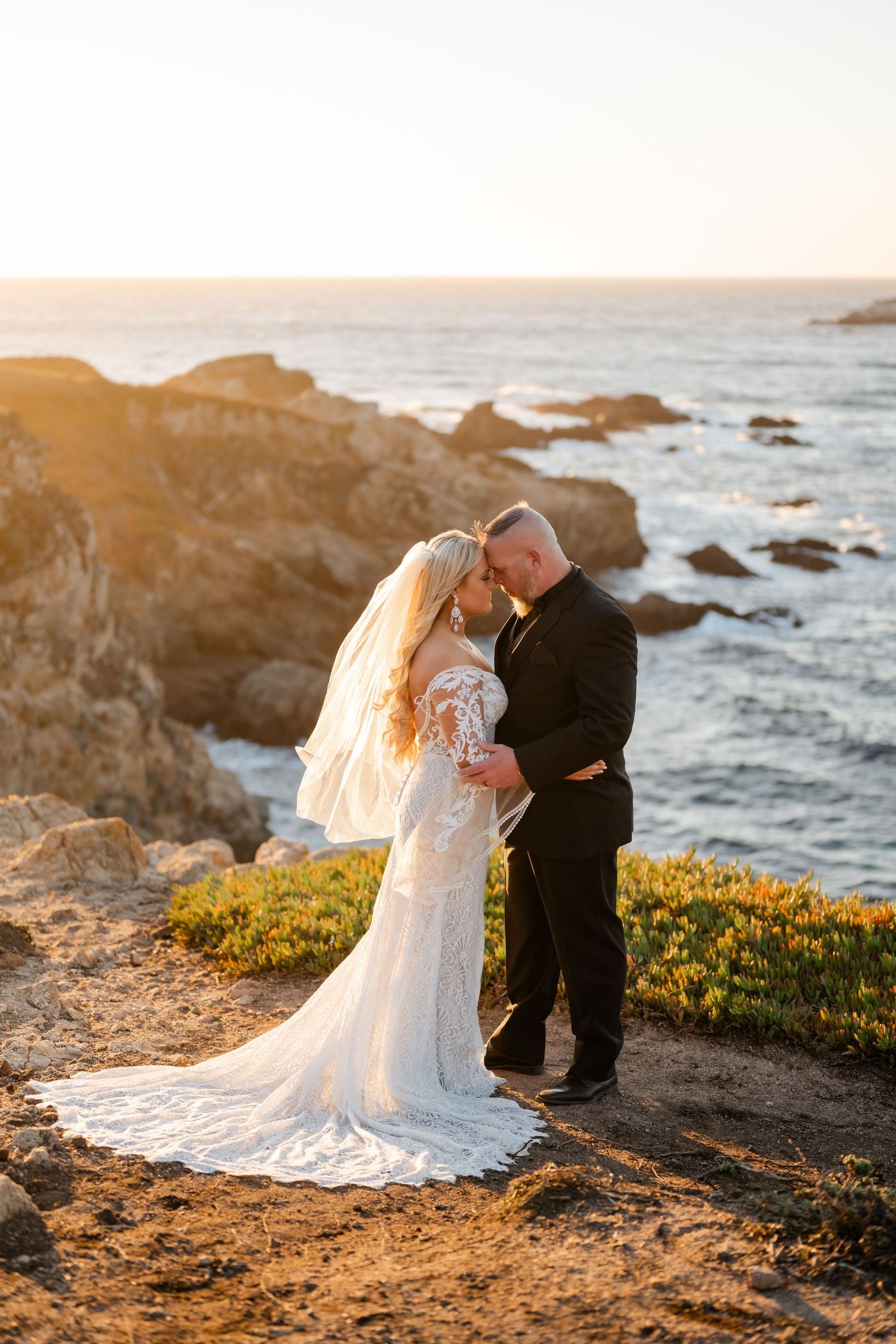 Romantic sunset wedding portraits on dramatic coastal cliffs with ocean backdrop.