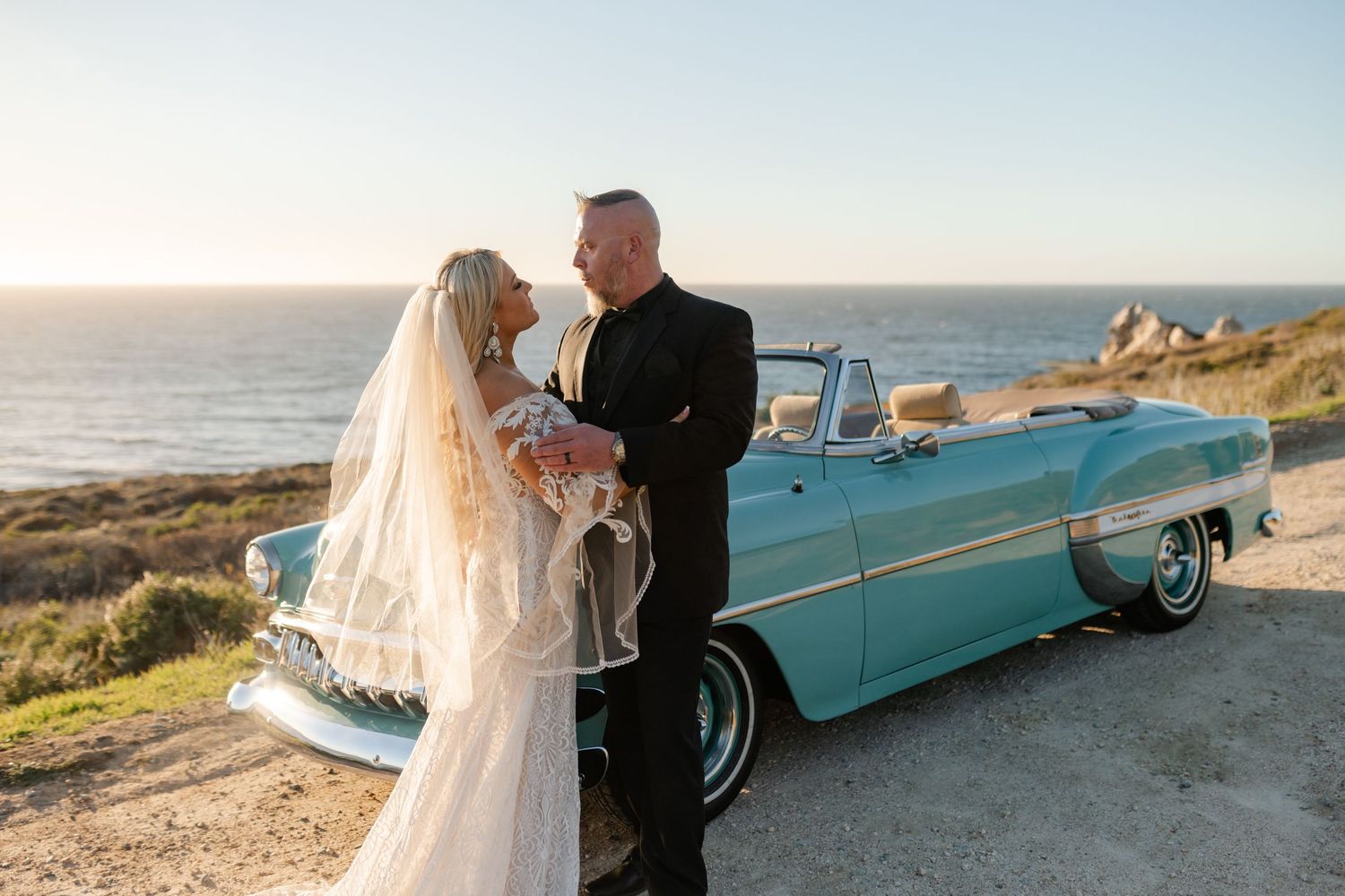 Seaside wedding photography with vintage turquoise convertible against coastal backdrop.