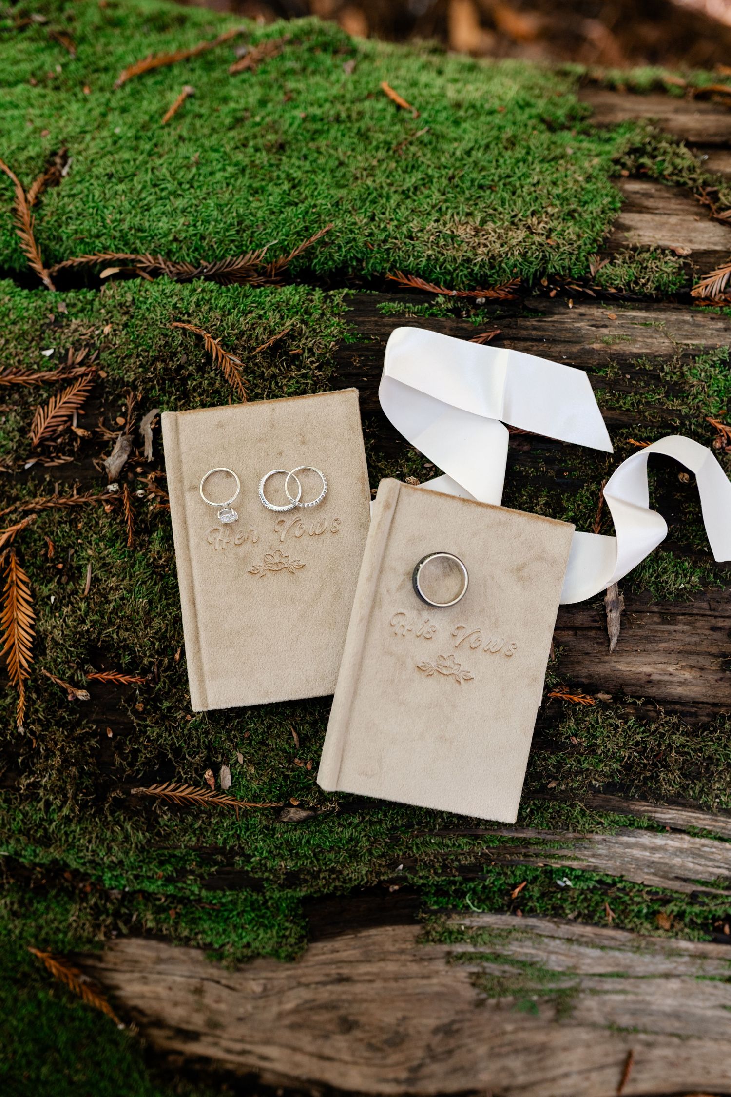 Wedding rings and details displayed on rustic wooden surface with green moss background.