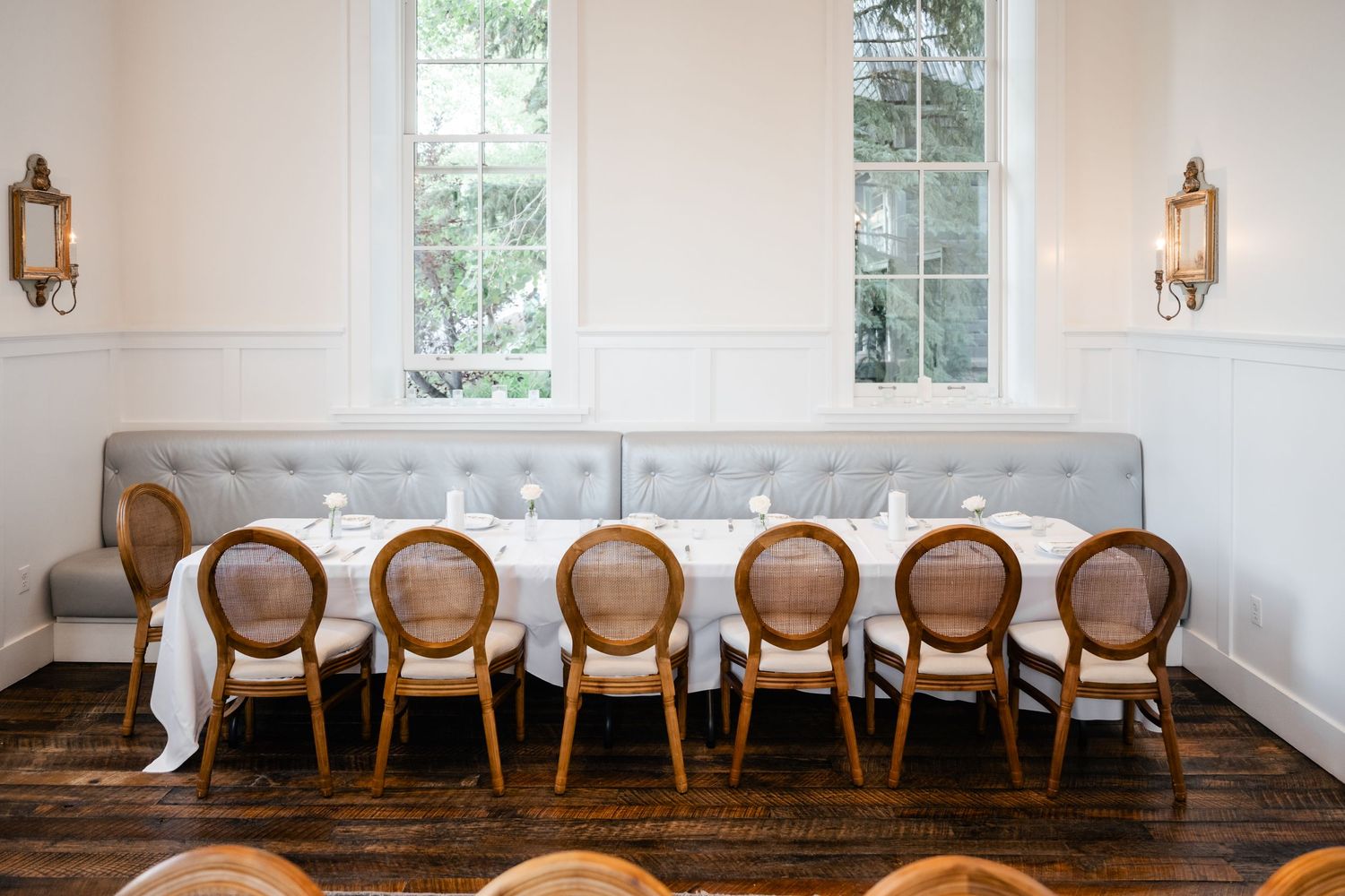 Row of elegant cane-back dining chairs lines a white wall with windows in an upscale event space.
