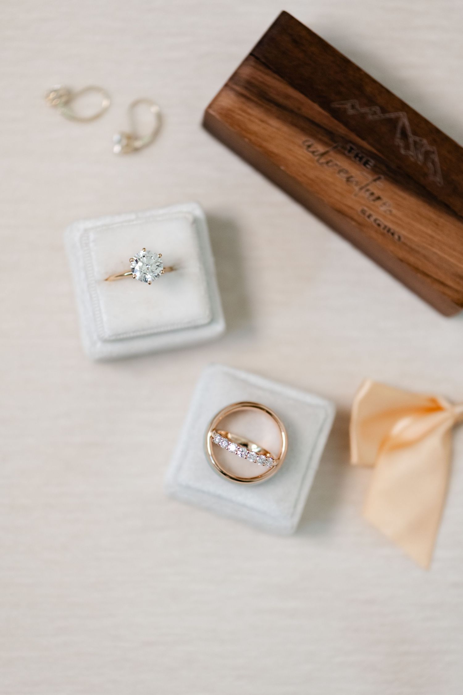 Wedding rings displayed in white ring boxes with a wooden box and peach ribbon accent.