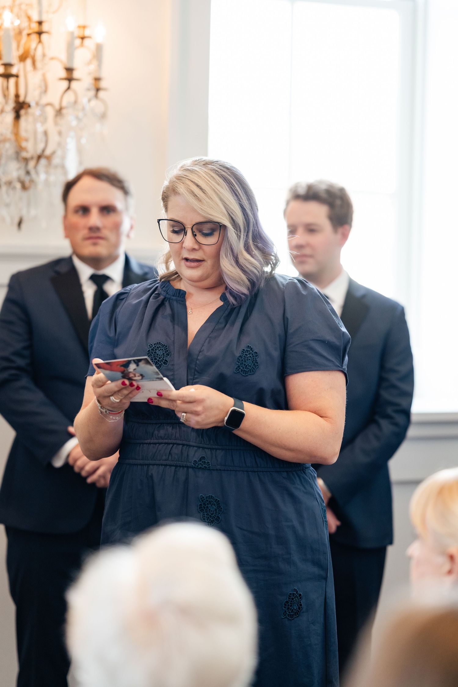 Wedding attendees in formal attire using phones to capture moments during ceremony.