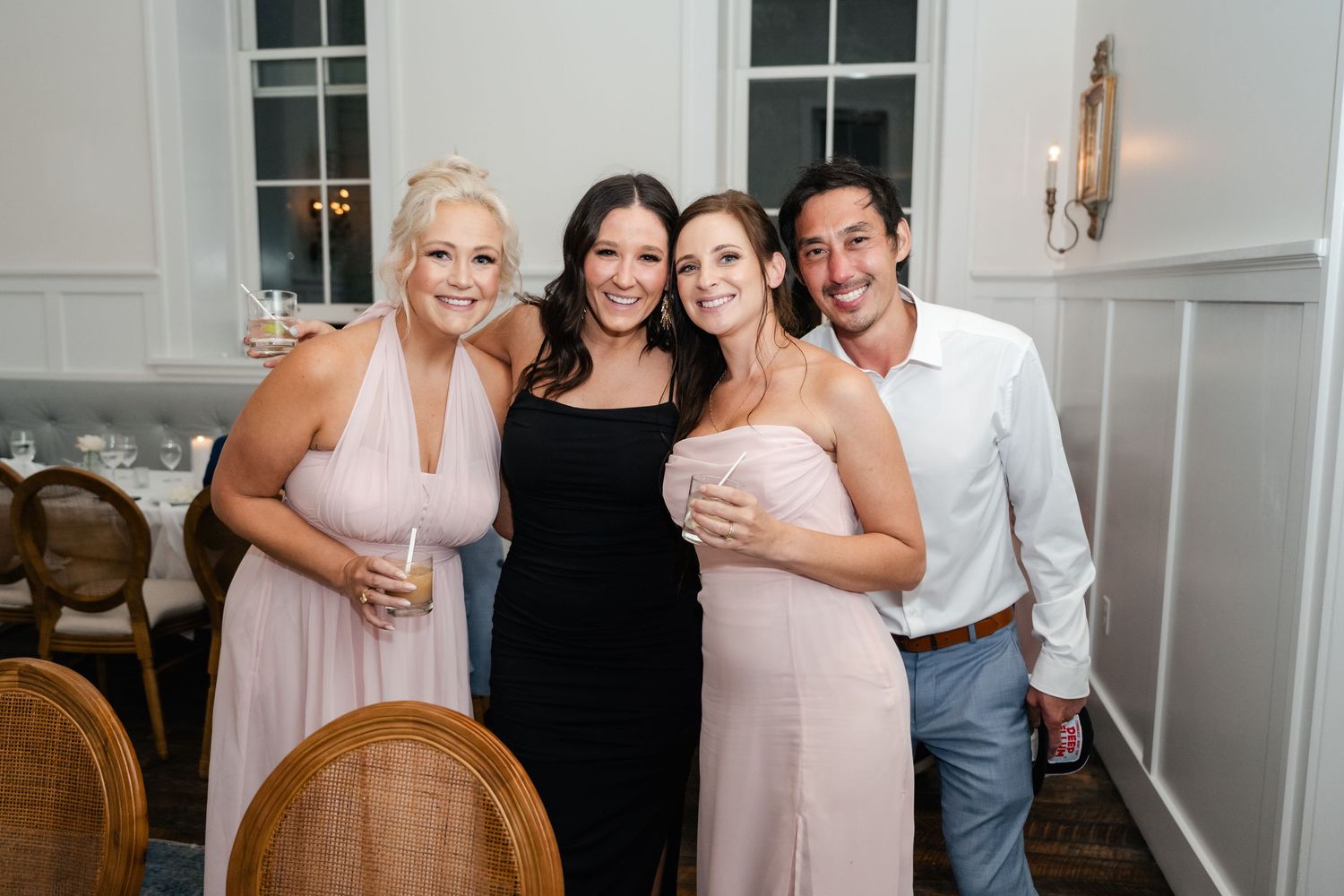 Wedding party members pose together in light pink and dark attire at an elegant indoor venue.