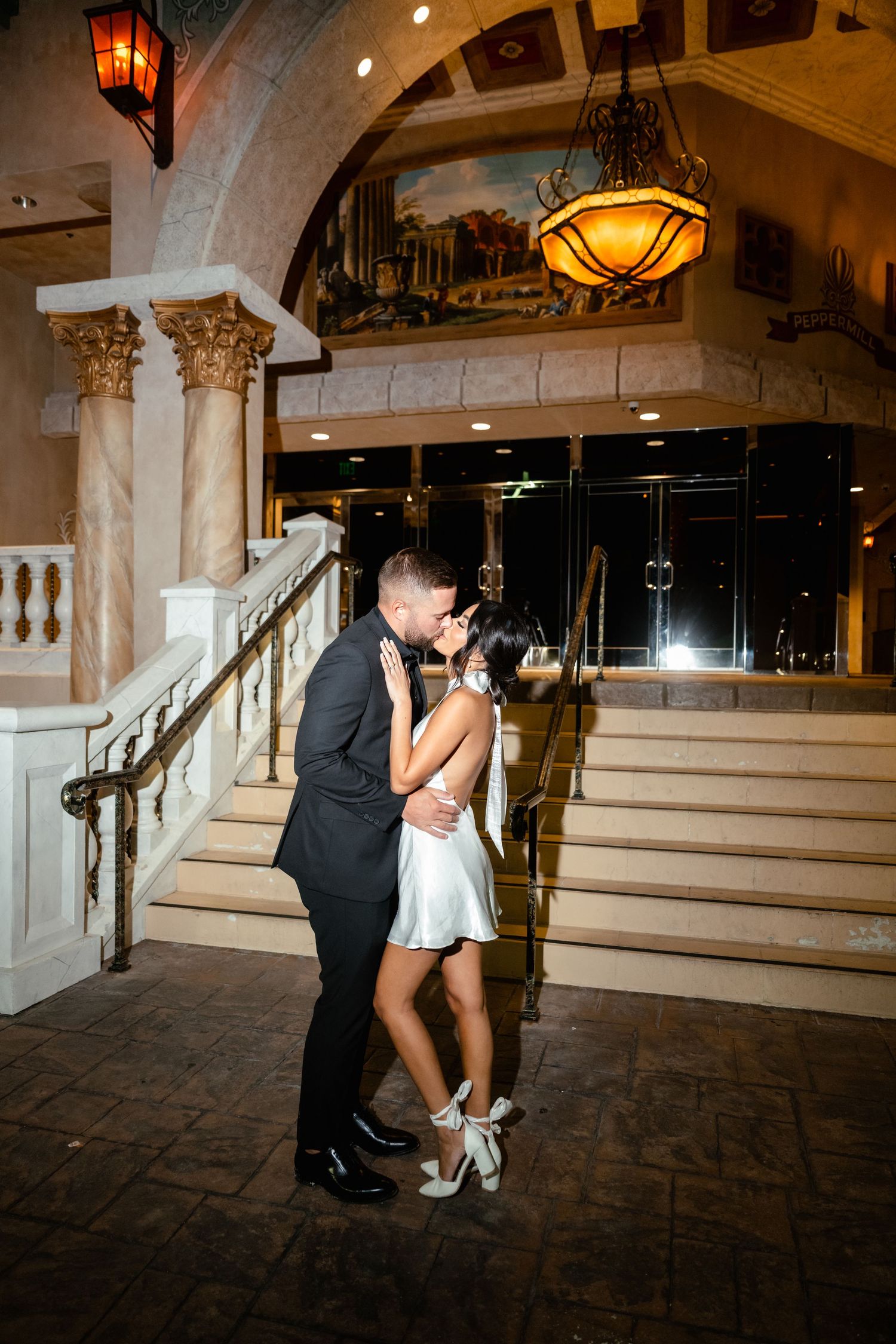Wedding couple shares romantic moment on ornate marble staircase with warm lighting.