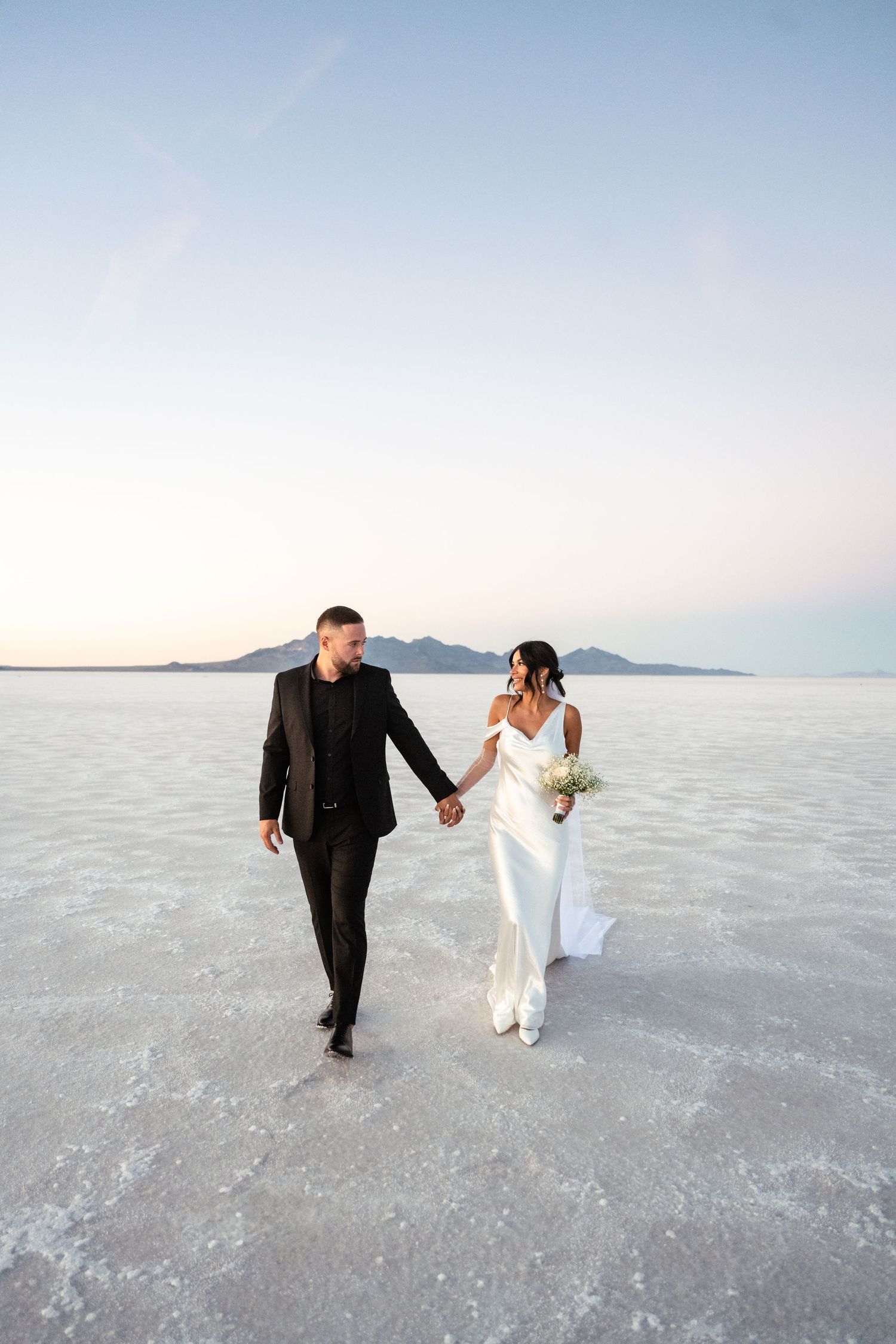Wedding couple walking together across stunning white salt flats landscape.