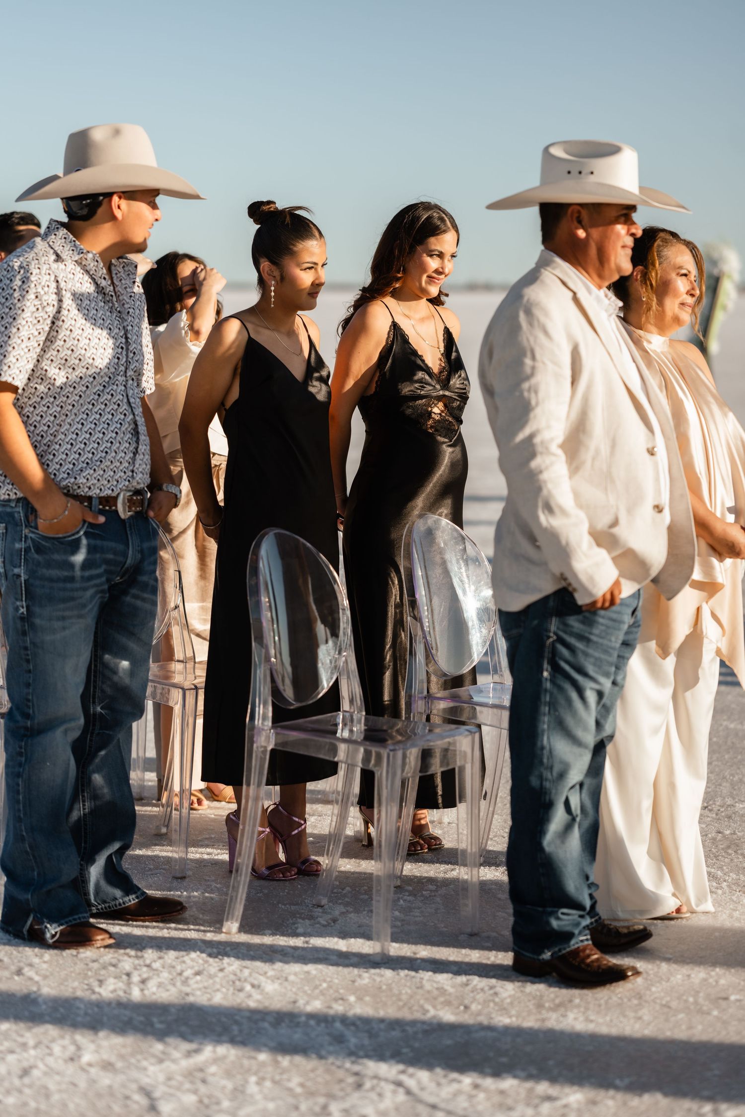 Wedding guests in casual attire gathered on a bright white sandy beach.