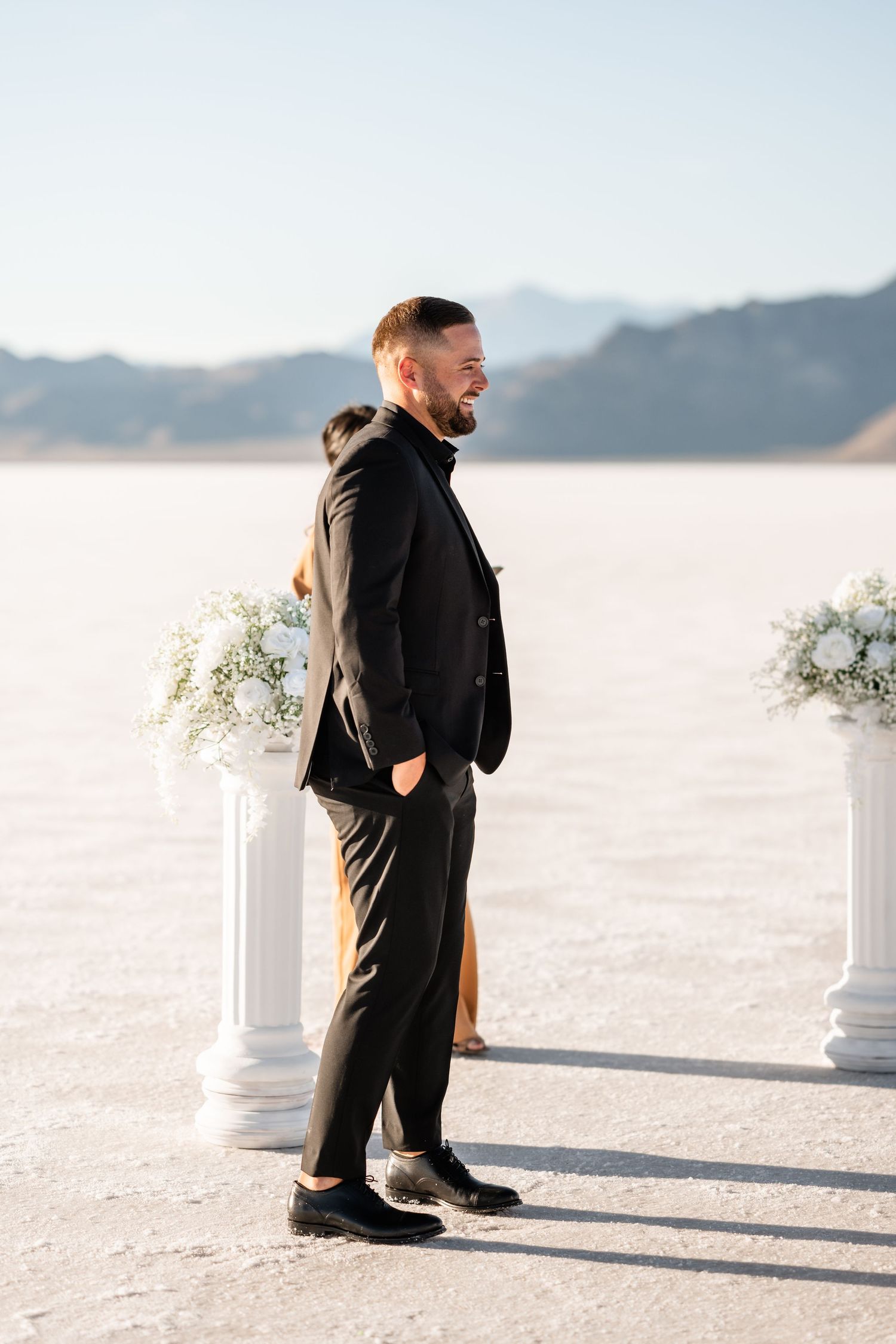 Wedding ceremony setup with white columns on a salt flat with mountains in the background.