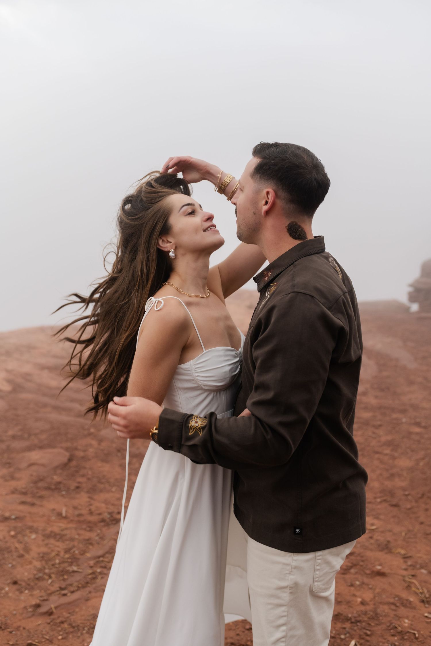 Joyful couple embracing on red desert rocks with wind blowing through their hair.