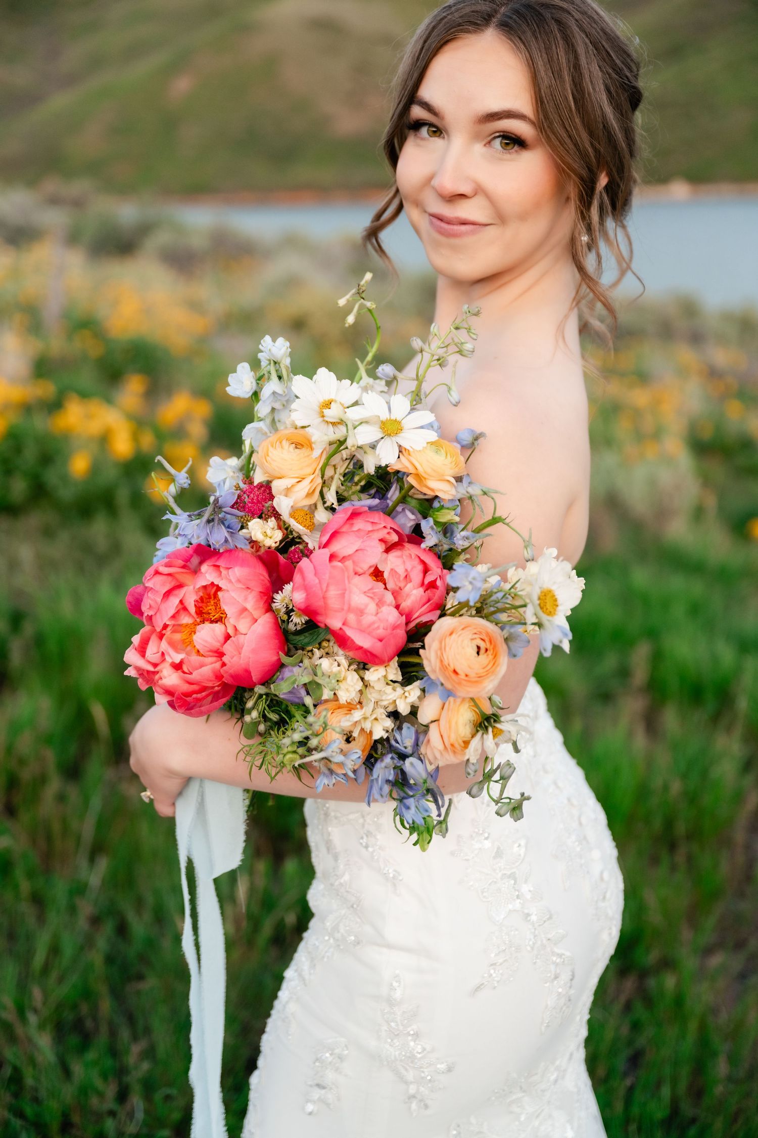 A stunning bridal bouquet features coral peonies, daisies and peach blooms against a natural outdoor backdrop.