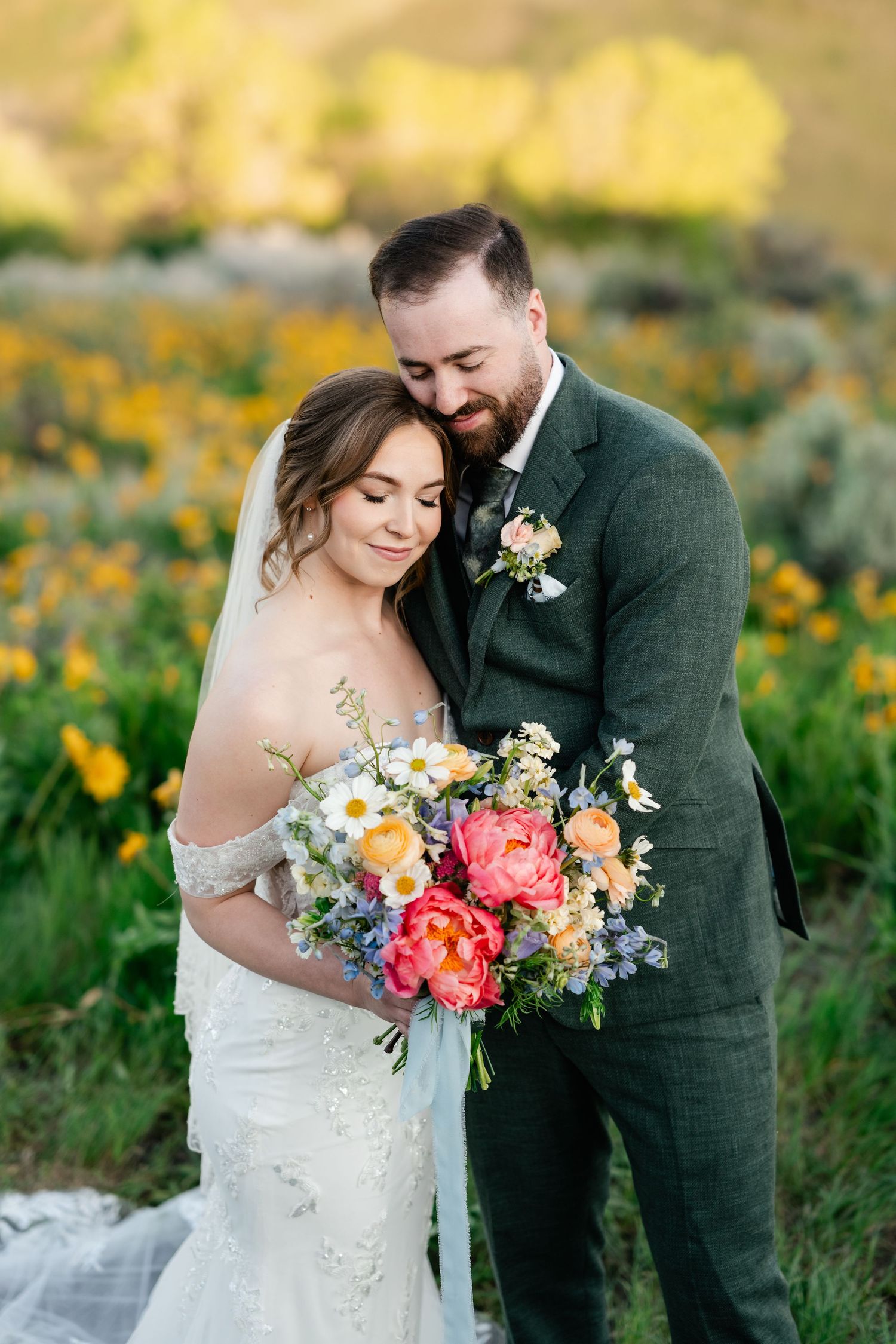 Couple shares intimate moment among wildflowers while holding vibrant spring bouquet.