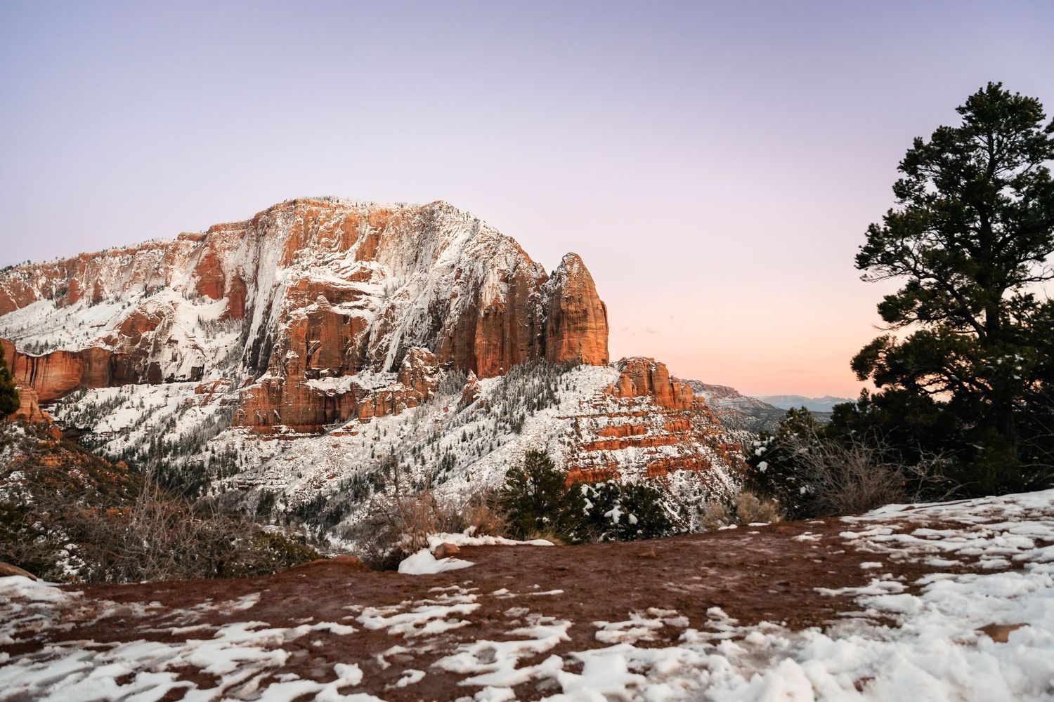 Snow-covered landscape of Zion National Park's iconic red rock formations at sunset.