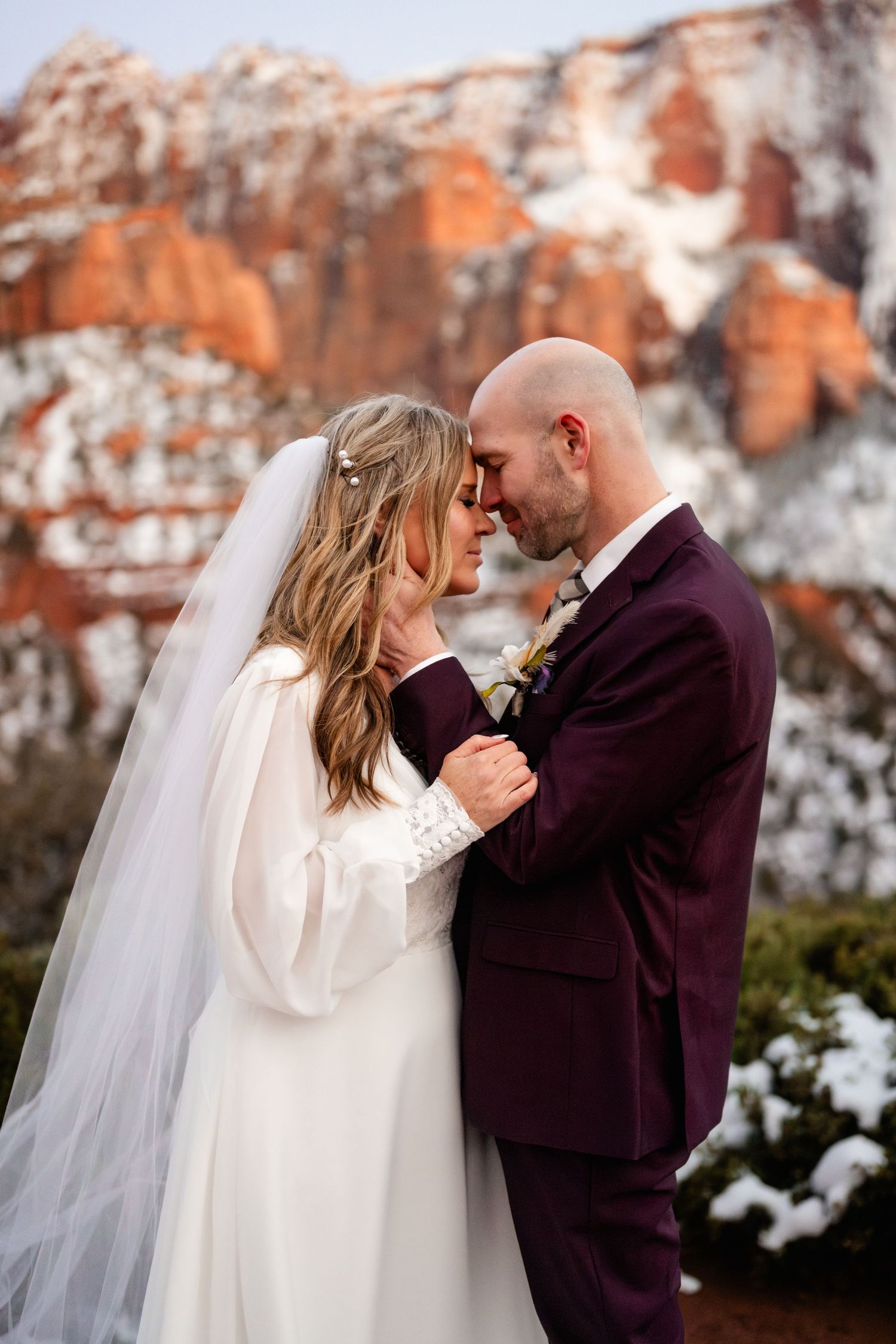 Intimate wedding moment captured against snow-covered red rock cliffs in winter.