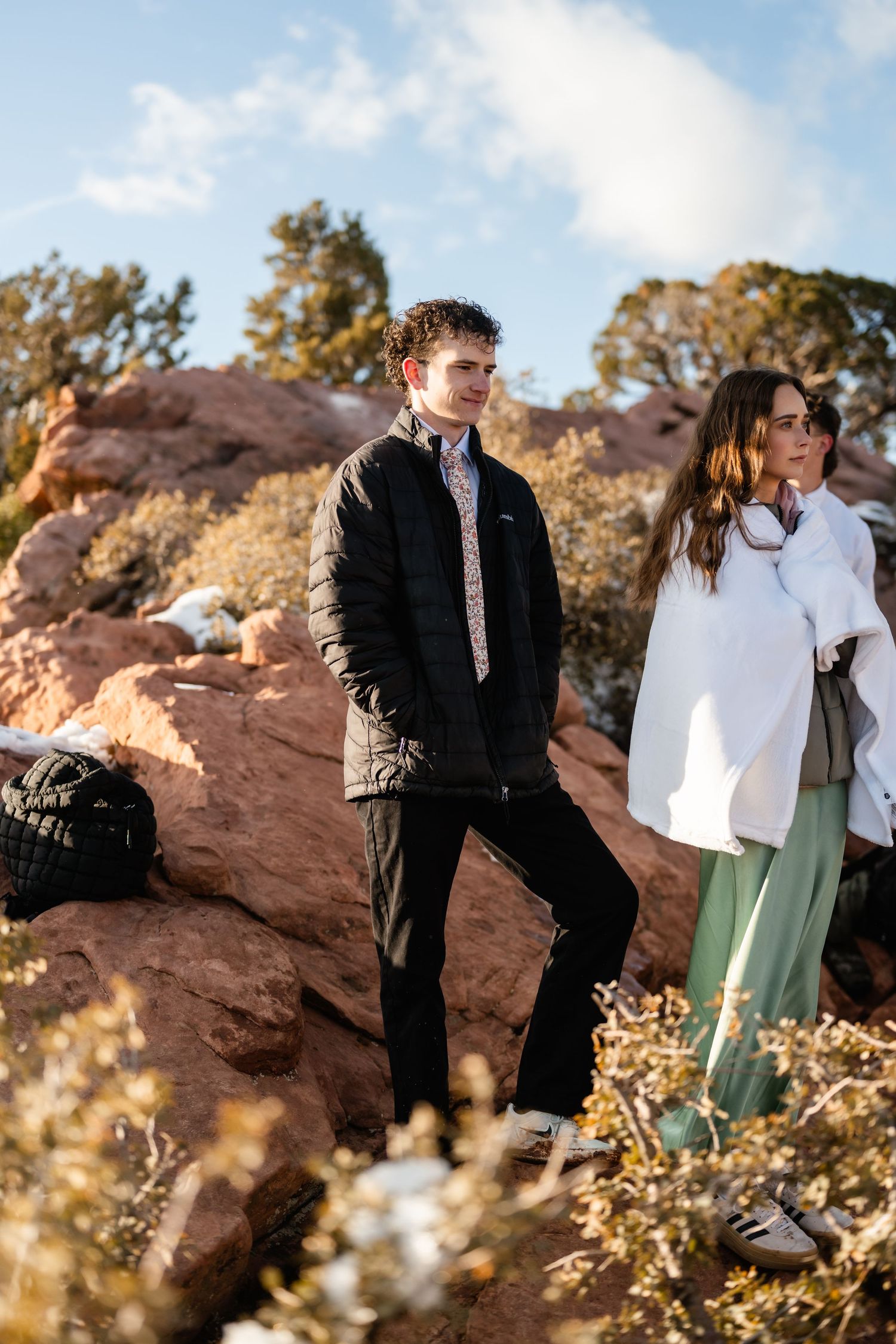A couple shares a romantic moment against red rock formations during a winter mountain photoshoot.