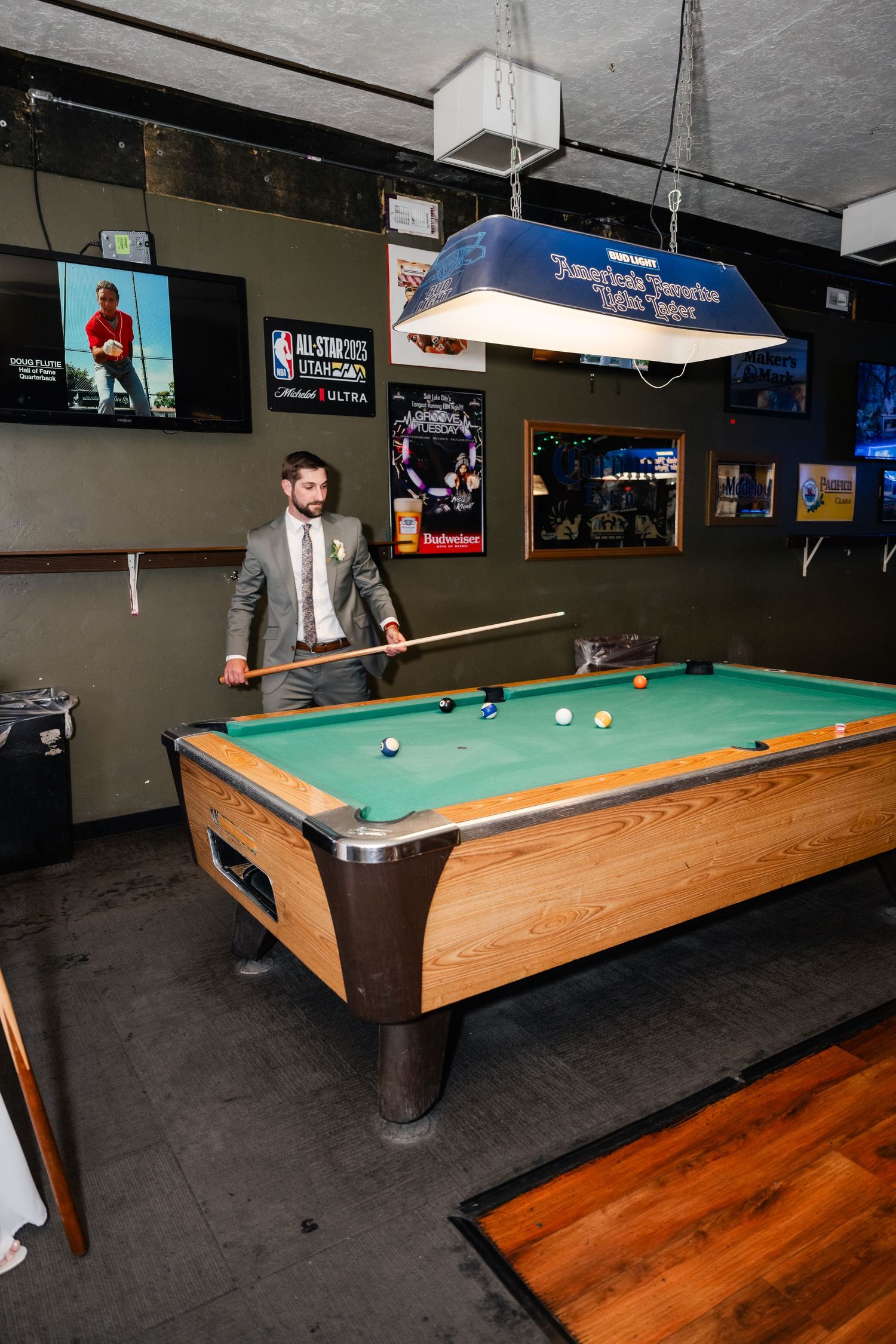 A person in formal attire plays pool at a bar with sports memorabilia on the walls.