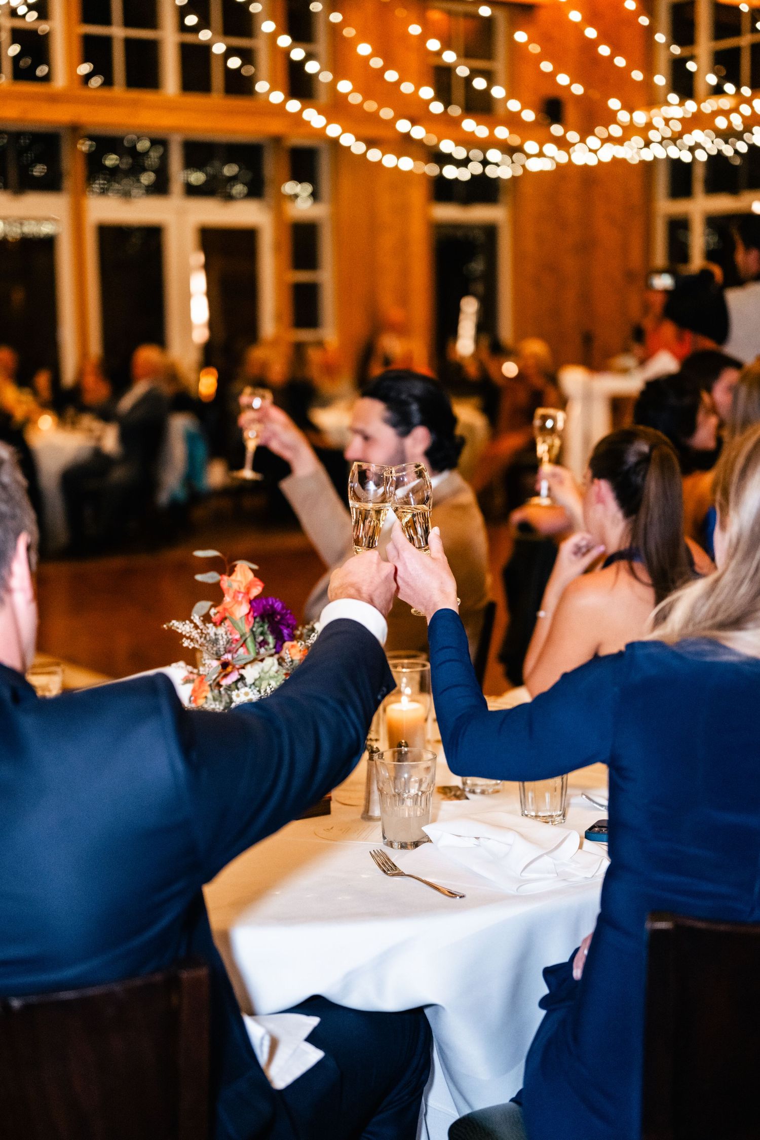 Wedding reception venue with string lights and guests seated at decorated tables.