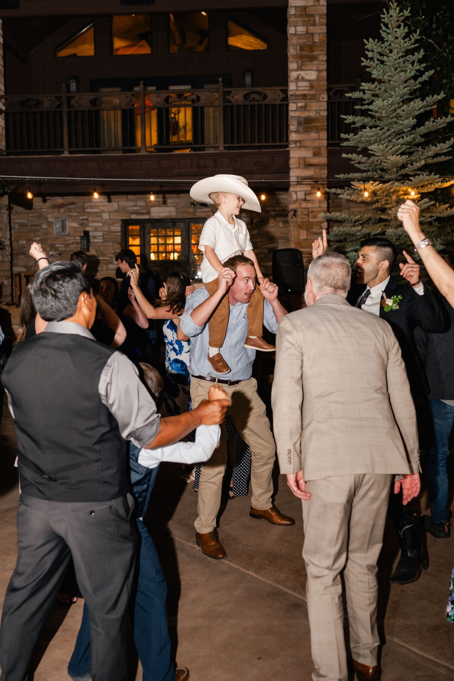 Wedding guests dancing and celebrating on an outdoor patio at night with stone building backdrop.