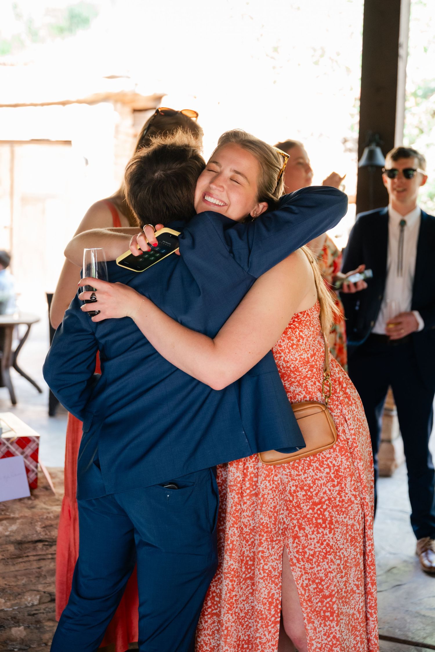 Wedding guests in formal attire embrace during an emotional moment at the reception.