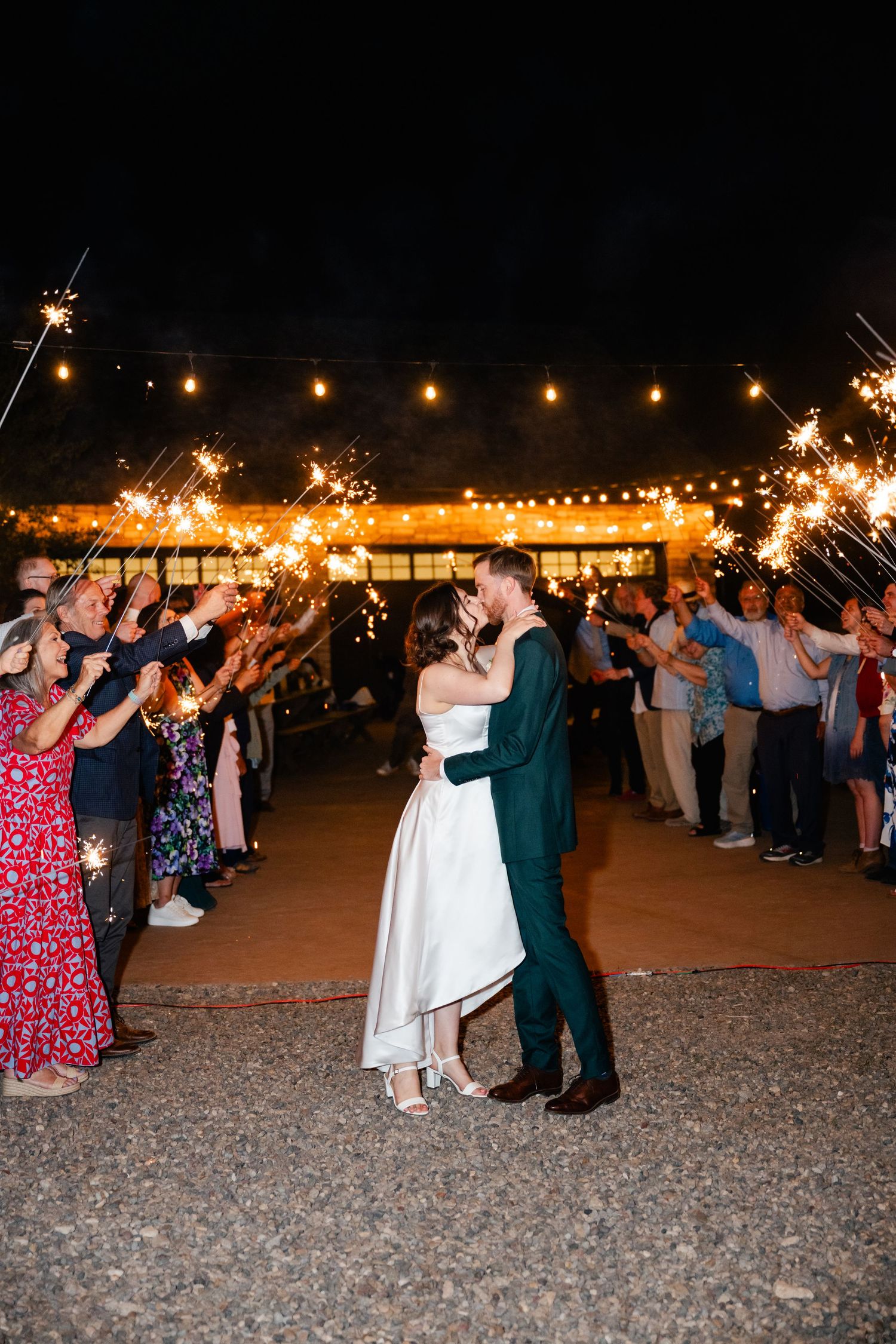 Wedding guests hold sparklers in a line creating a magical nighttime send-off for the newlyweds.