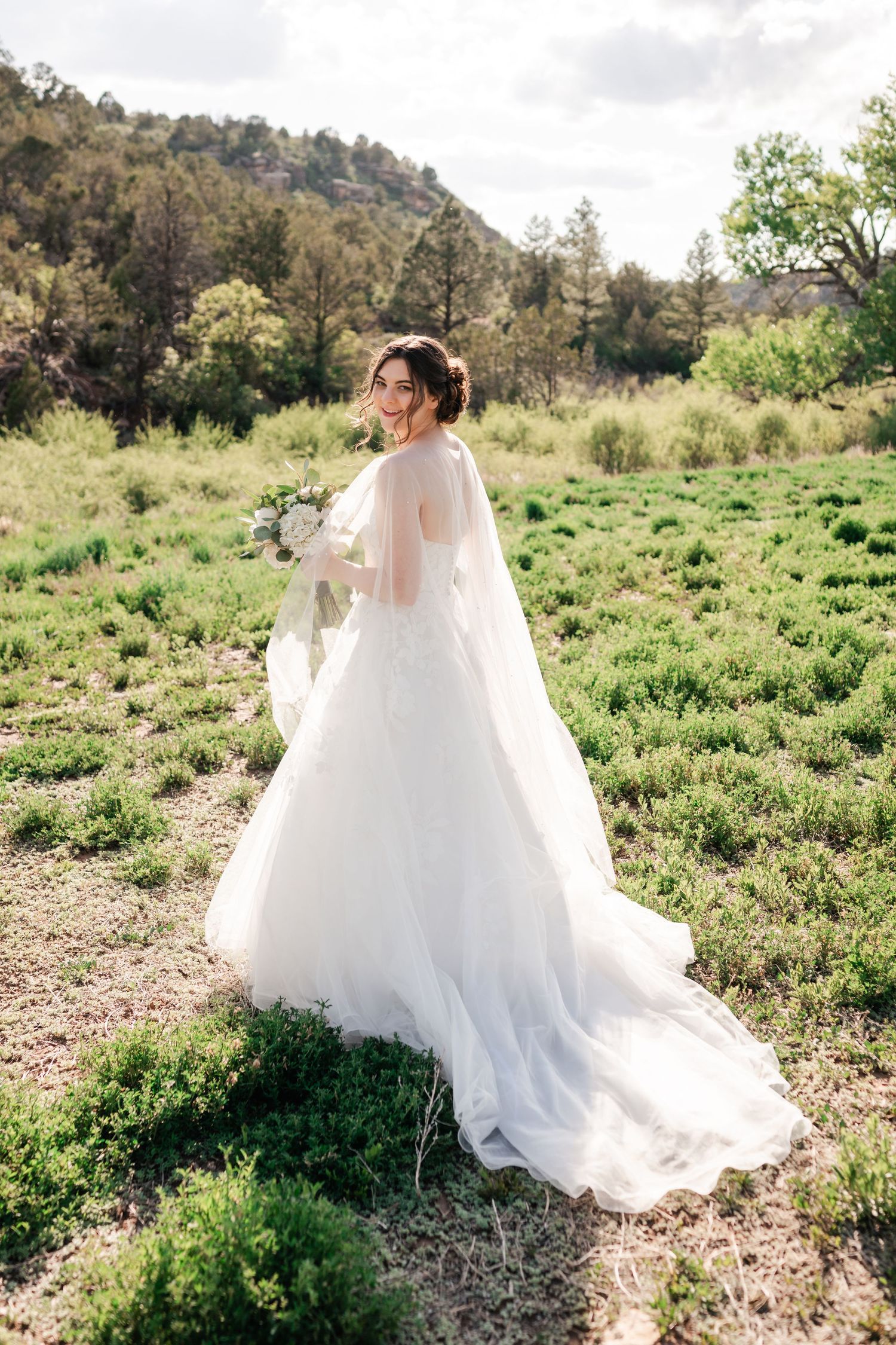A flowing white wedding dress creates movement against a natural mountain landscape.