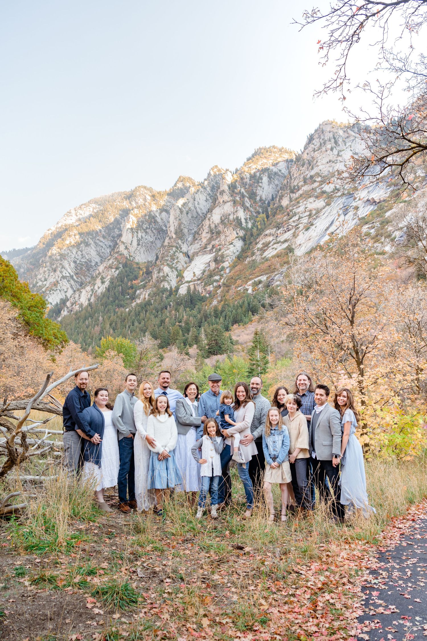 A group of people gathered outdoors in front of scenic mountain landscapes during autumn with fallen leaves on the ground.