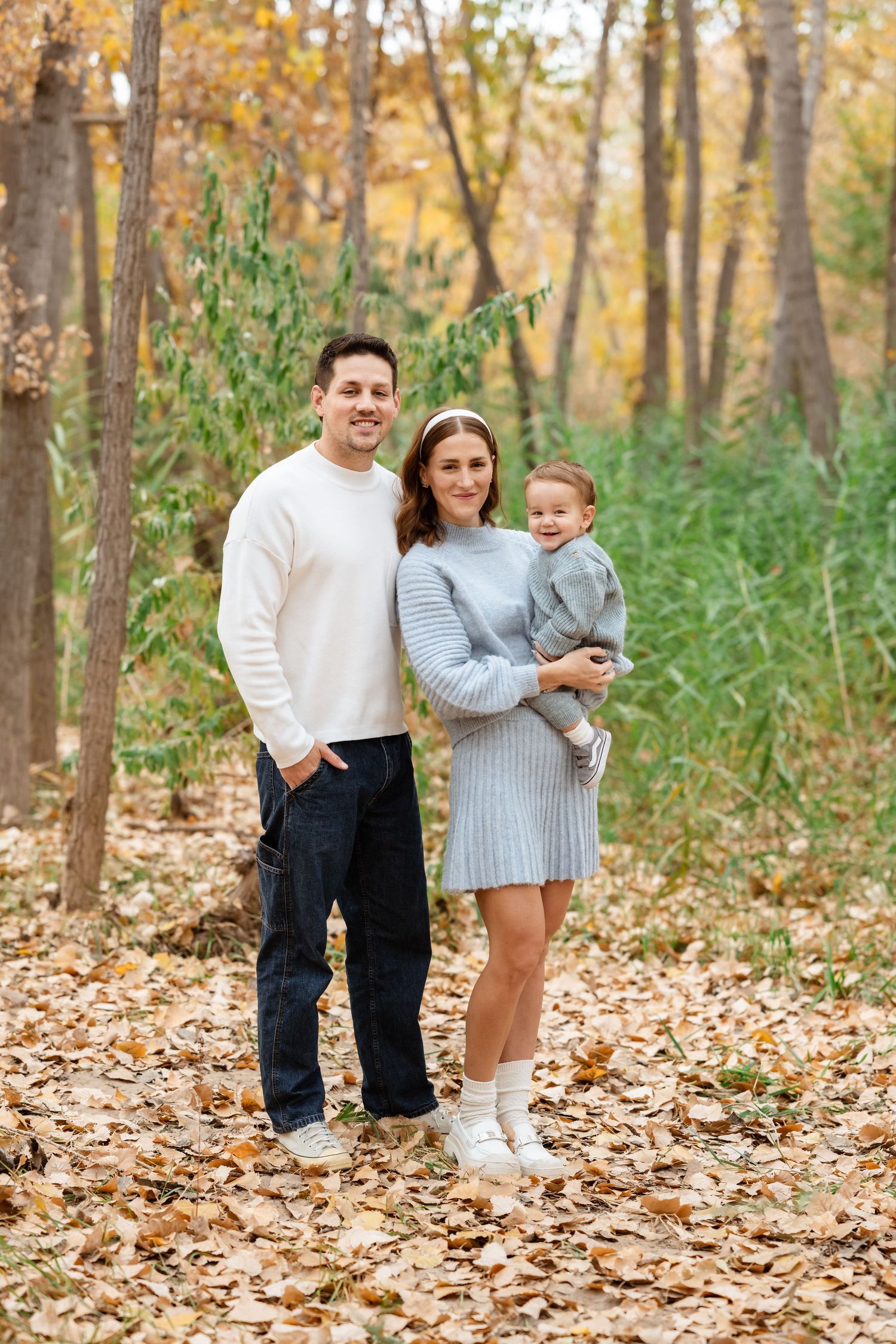 A family walking through fallen autumn leaves in a wooded area during a fall photo session.