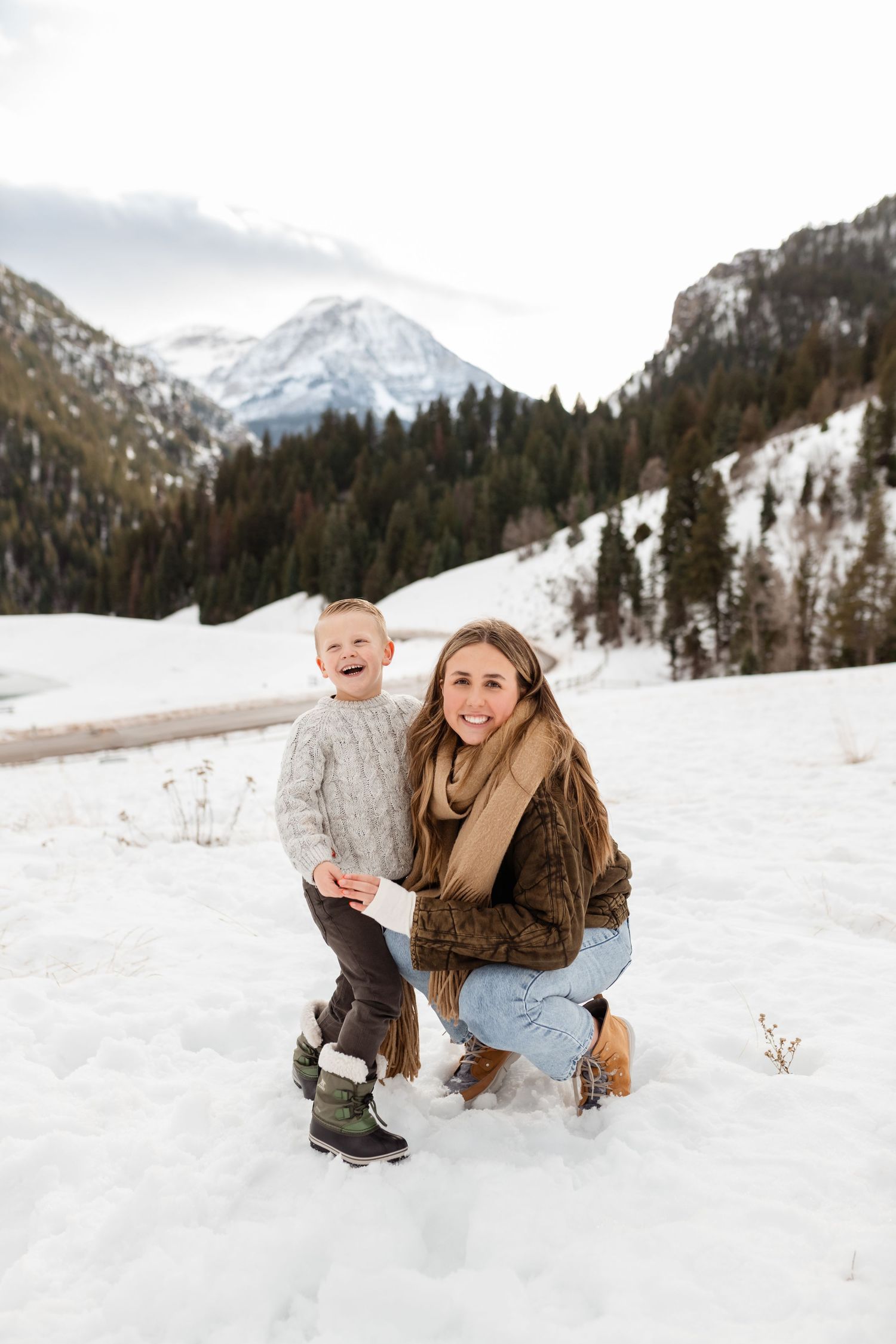 A snowy winter photoshoot in the mountains with people enjoying the pristine white landscape against evergreen trees.