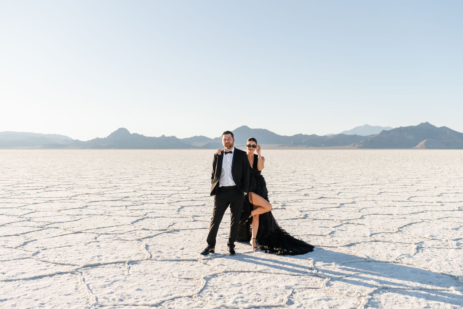Salt Flats Elopement Photographer. Couple in formal attire poses for wedding photos on white salt flats with mountains in the background.