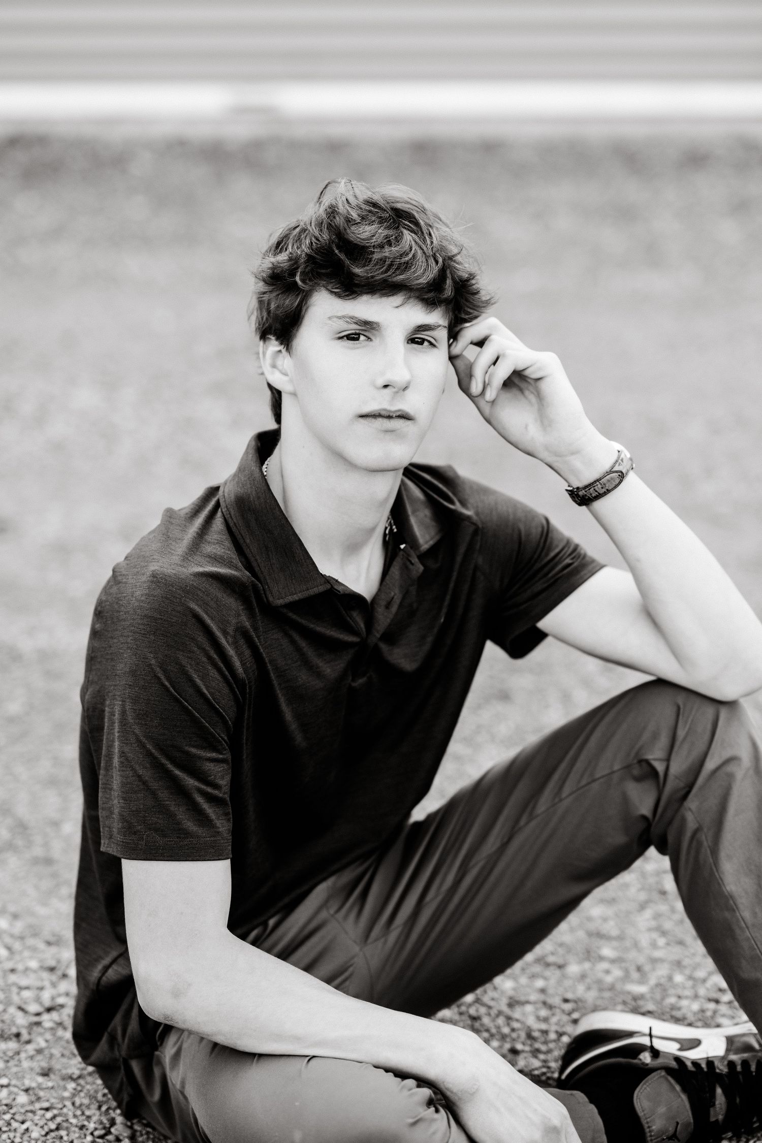 Black and white portrait of a young person in a polo shirt sitting outdoors with a thoughtful expression.