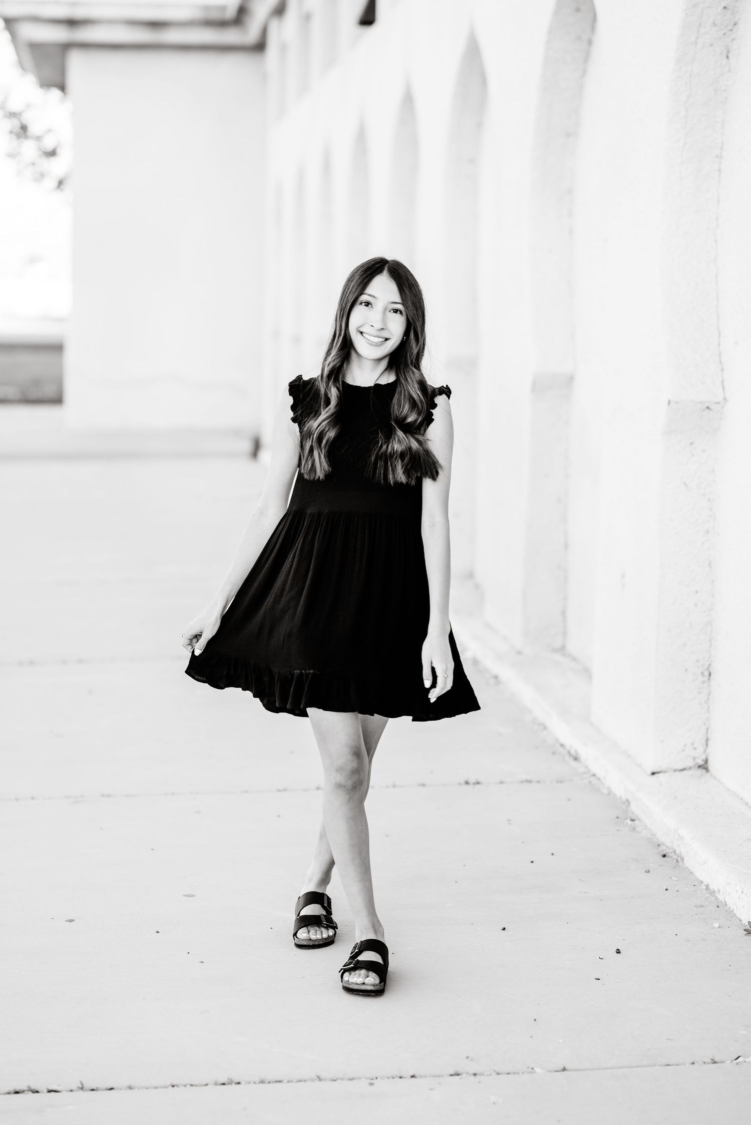 Black and white photo series showing a young child in a black dress twirling and playing against a white wall.