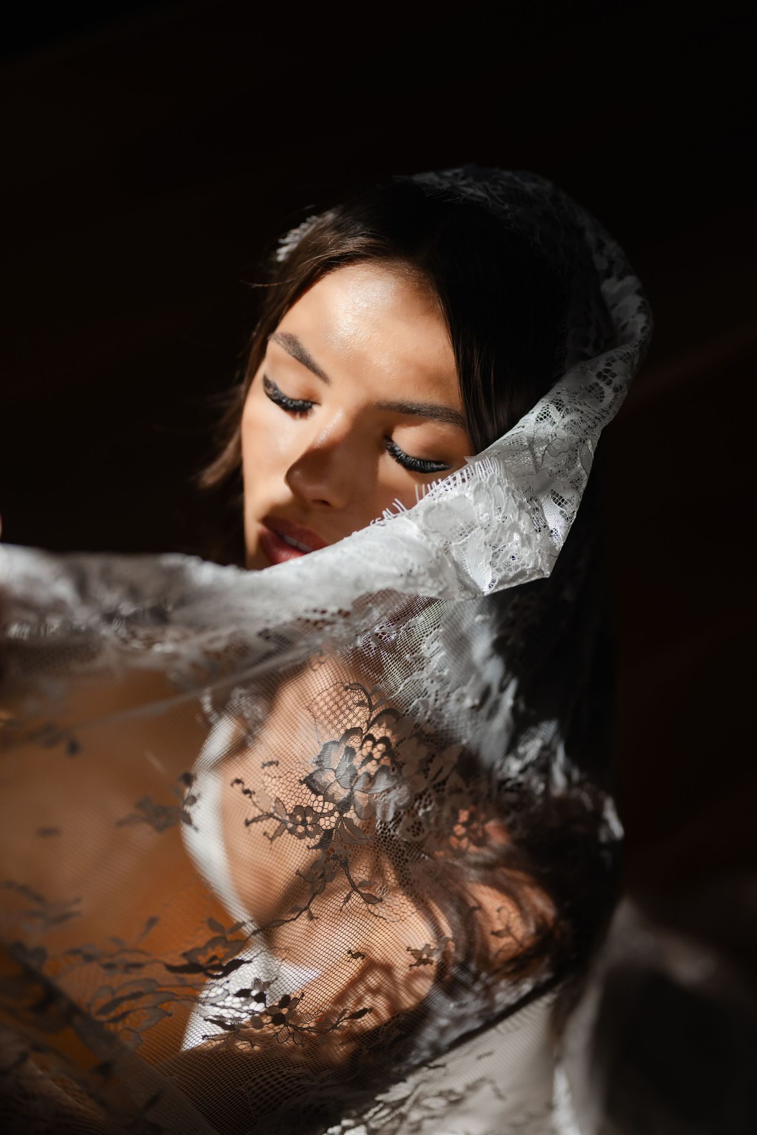 A woman with closed eyes draped in delicate black and white lace fabric, posed in dramatic chiaroscuro lighting.