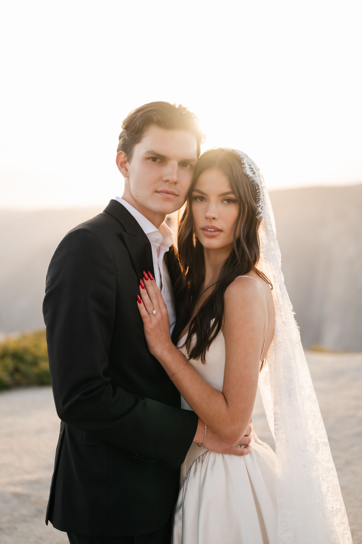Bride and groom embrace in golden sunset light on rocky mountain overlook during elopement.