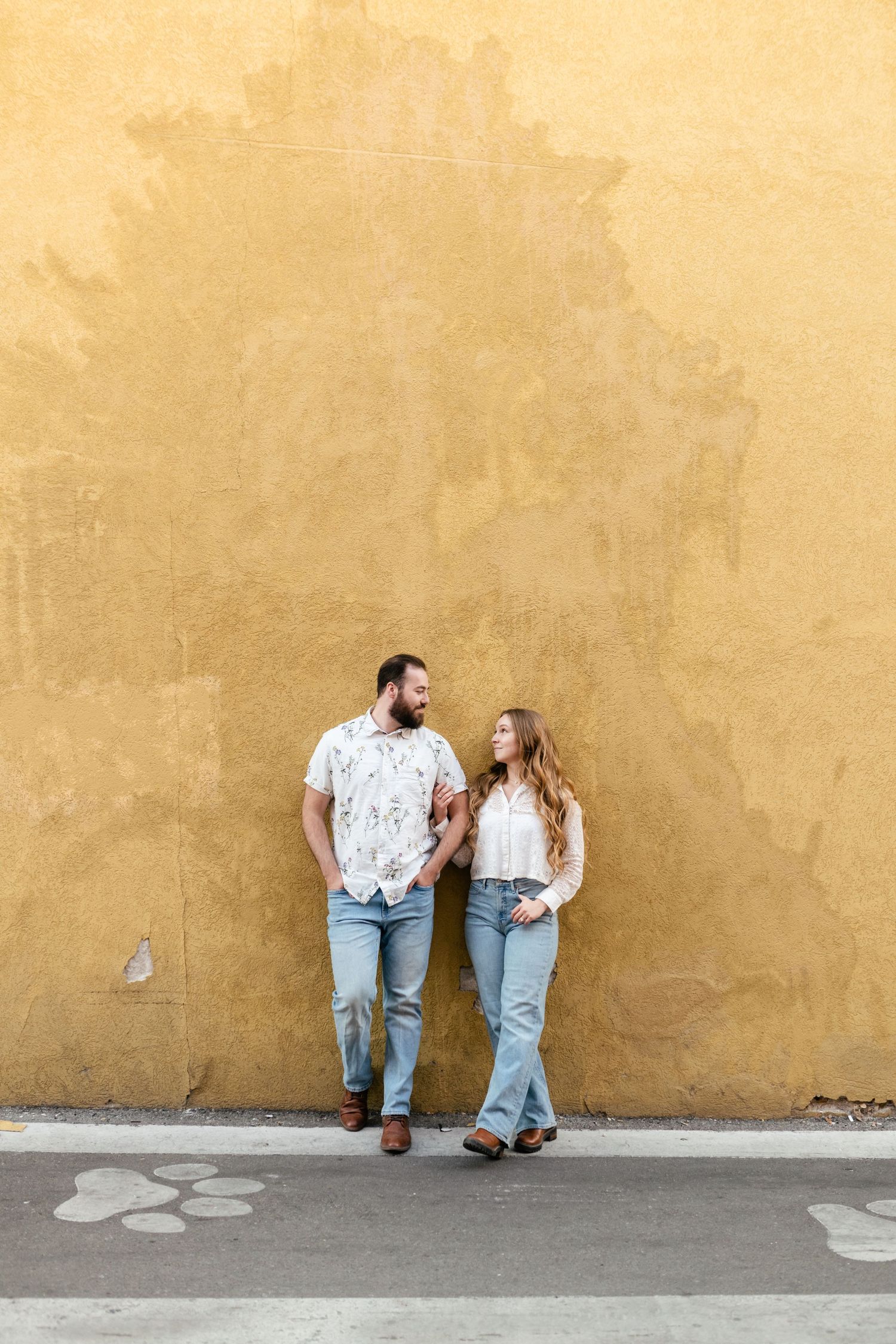 A couple in casual attire leans against a yellow wall in a series of candid poses. Park City Engagement Photographer.
