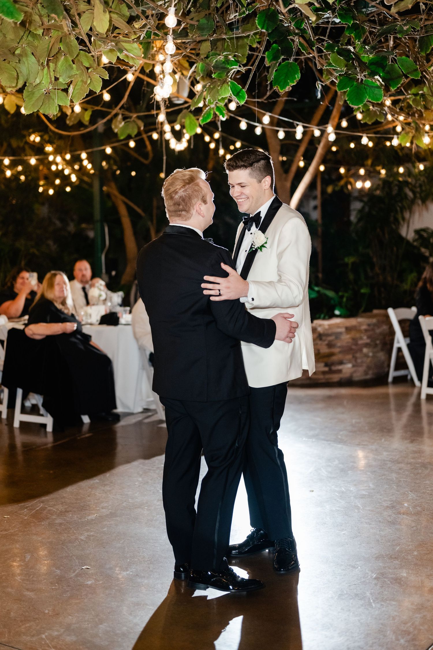 A couple shares a romantic dance moment on an illuminated dance floor beneath twinkling lights and greenery at Highland Gardens.