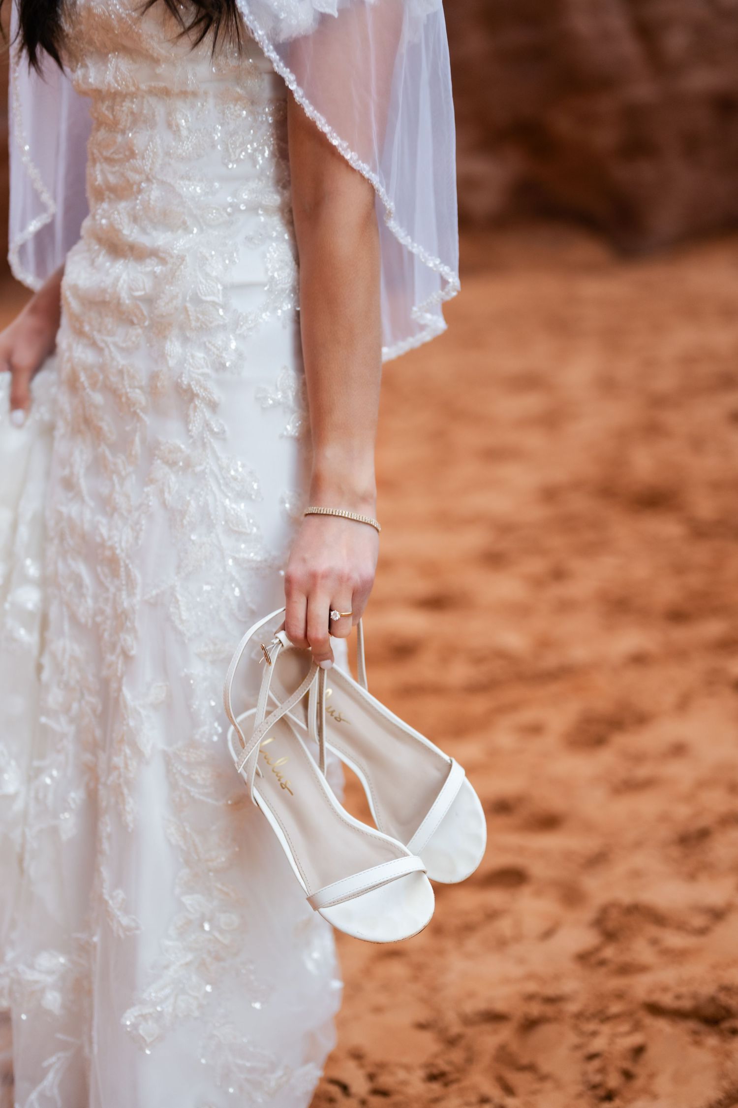 White wedding heels held against a red desert landscape backdrop.
