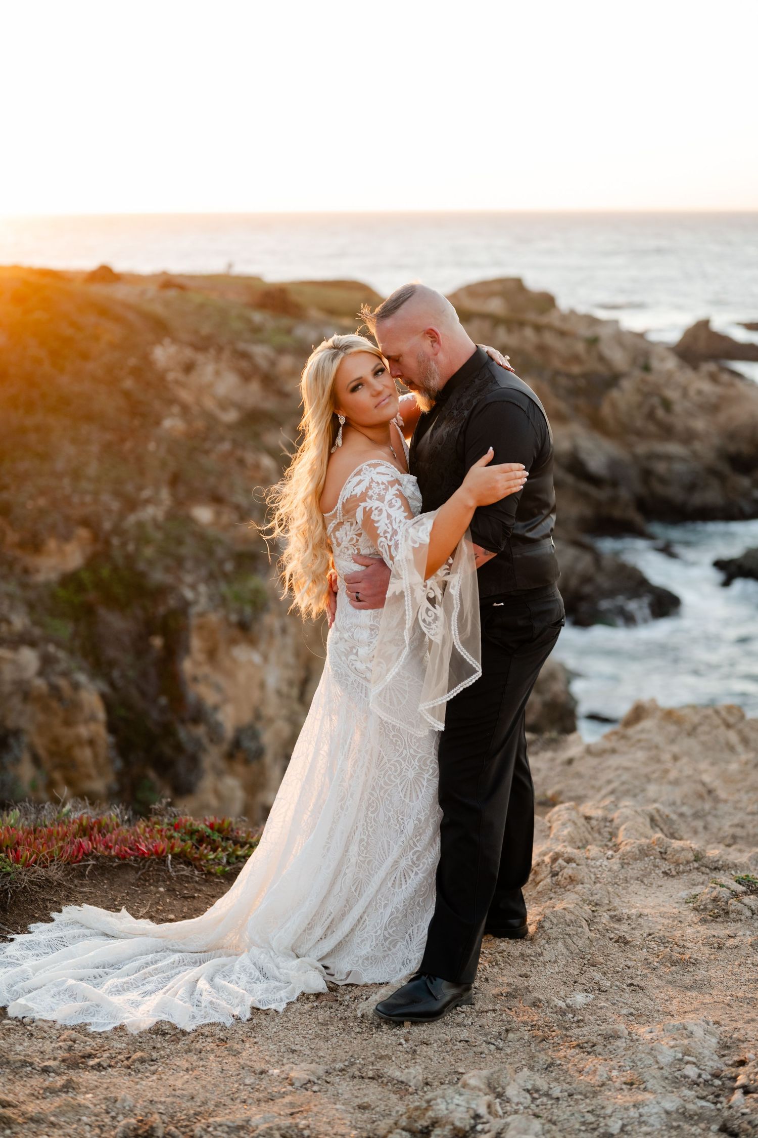 A romantic sunset wedding portrait captured on rocky coastal cliffs overlooking the ocean.