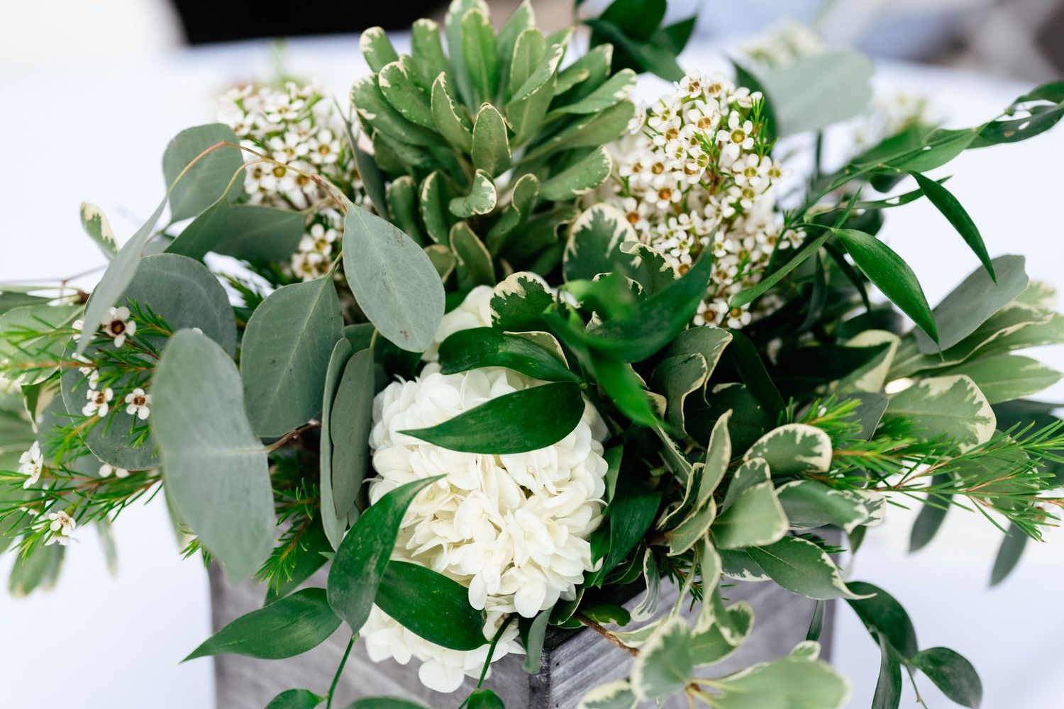 Fresh green and white floral arrangement with delicate blooms and foliage displayed in a horizontal layout.