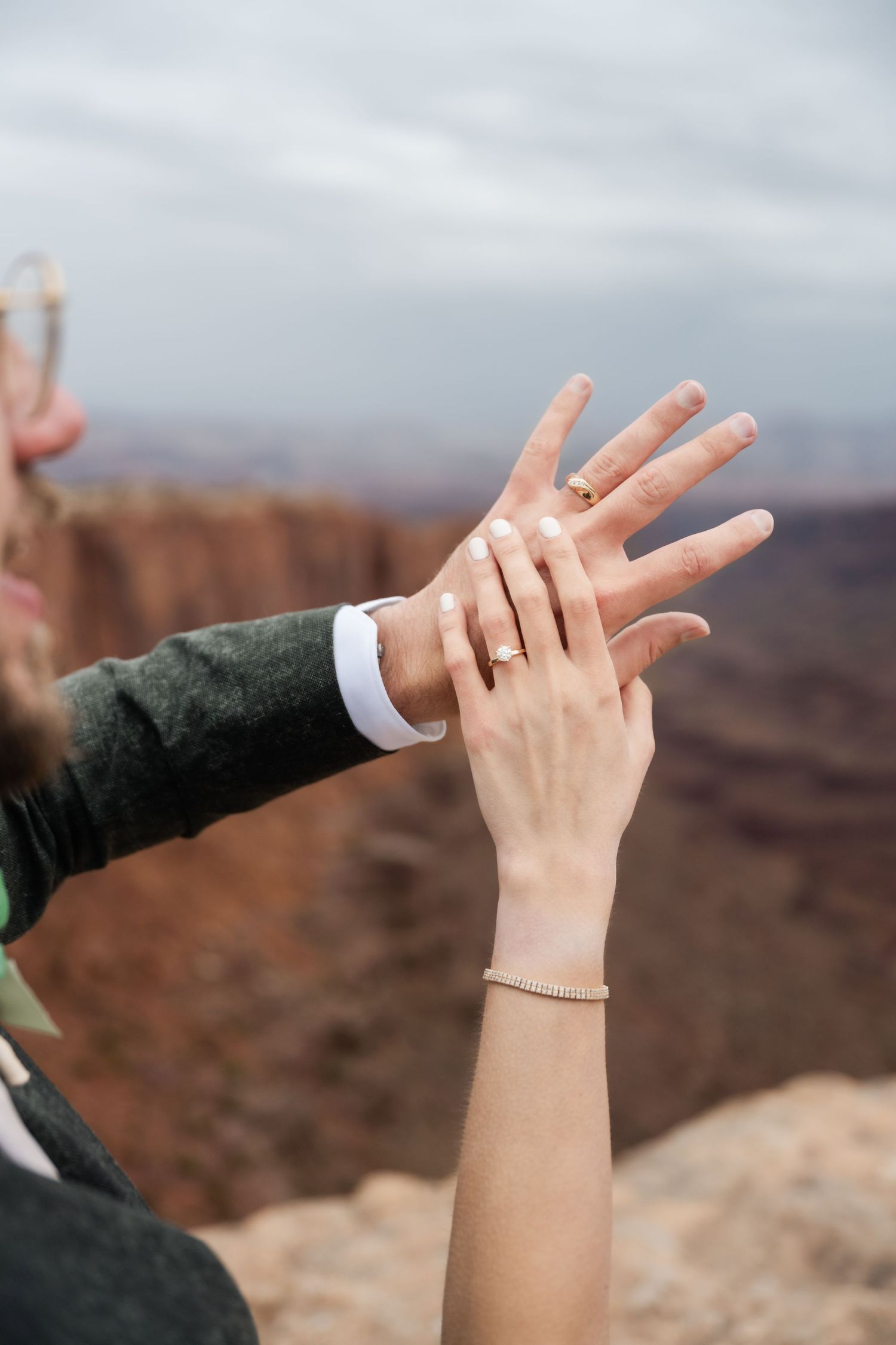 Two hands display wedding rings against a dramatic canyon backdrop.