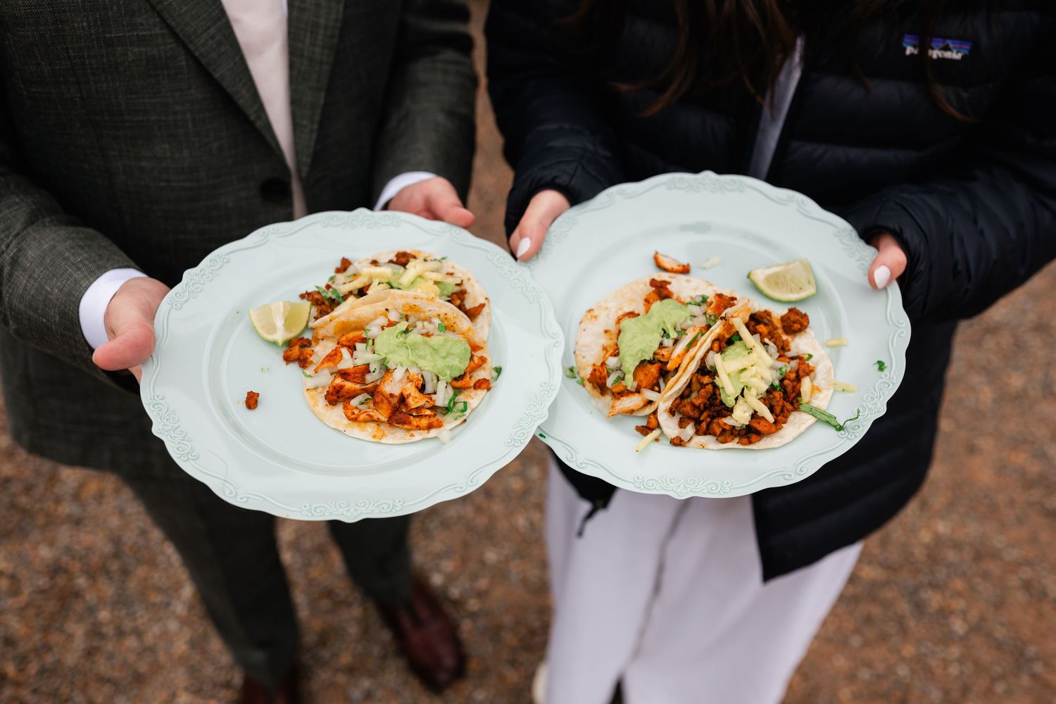 White plates of fresh tacos garnished with herbs and toppings being served at a catered event.