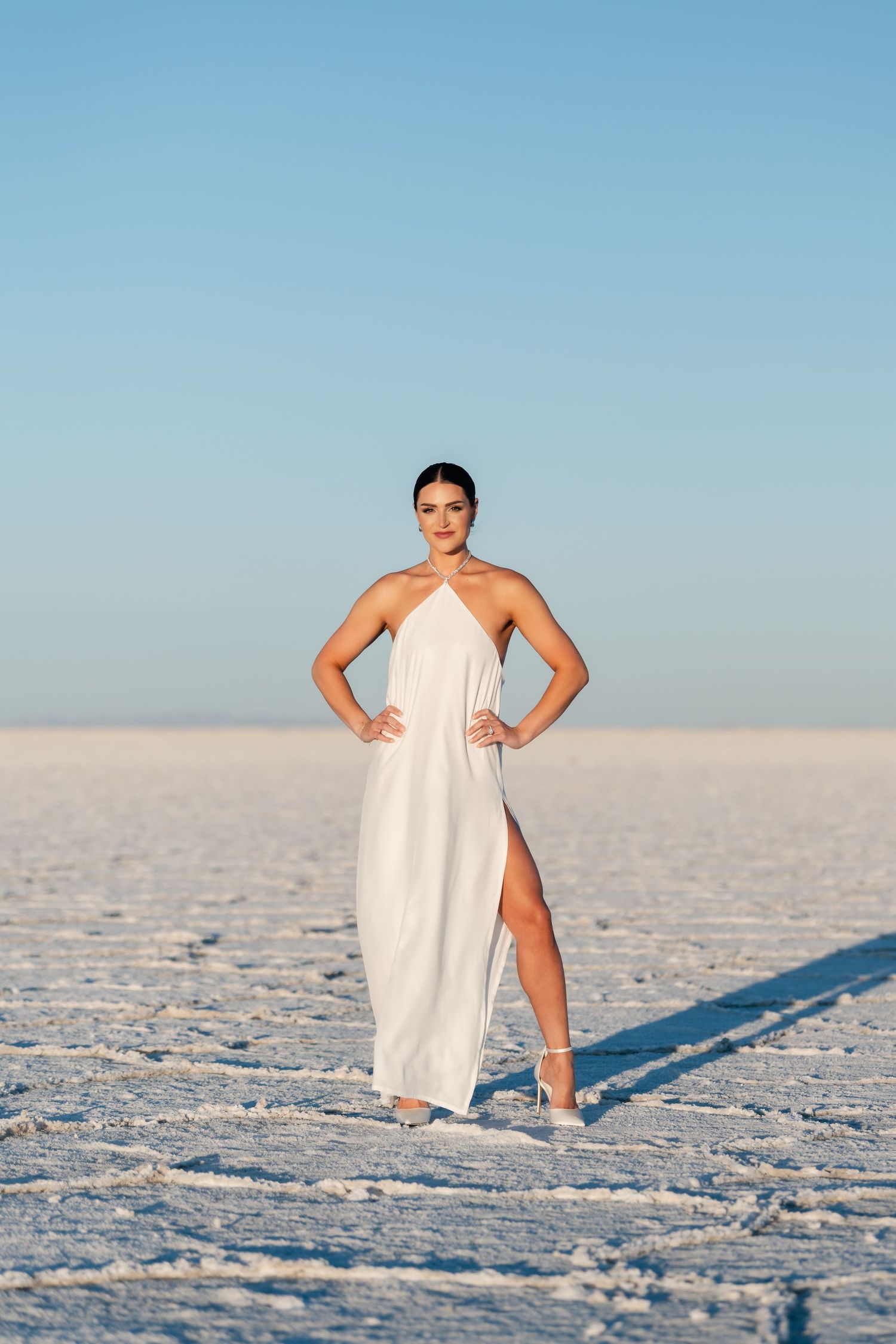 Salt Flats Photographer. A figure in a flowing white dress poses gracefully on the crystalline salt flats during a bright sunny day.