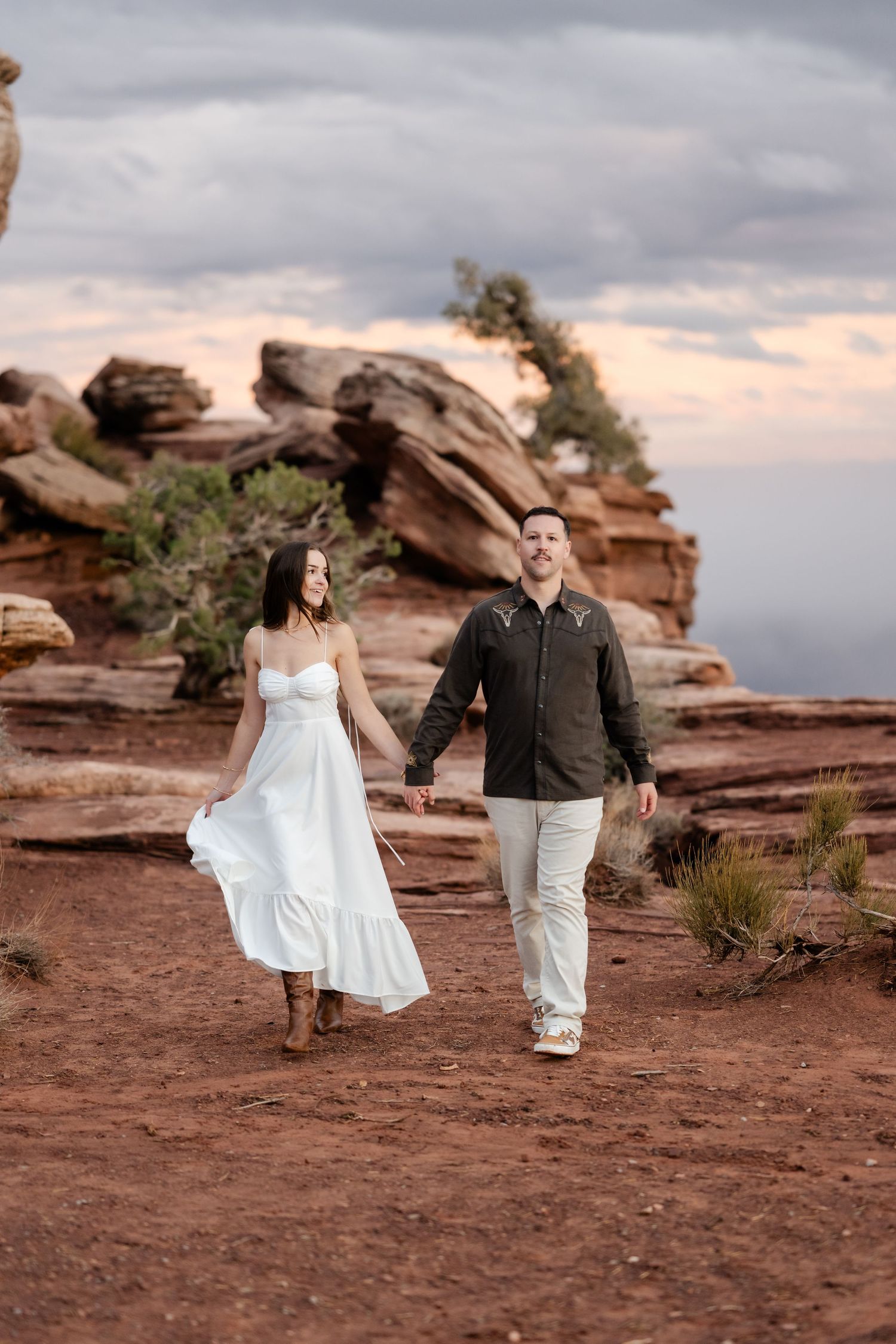 Couple walking hand in hand across red desert rocks during golden hour.