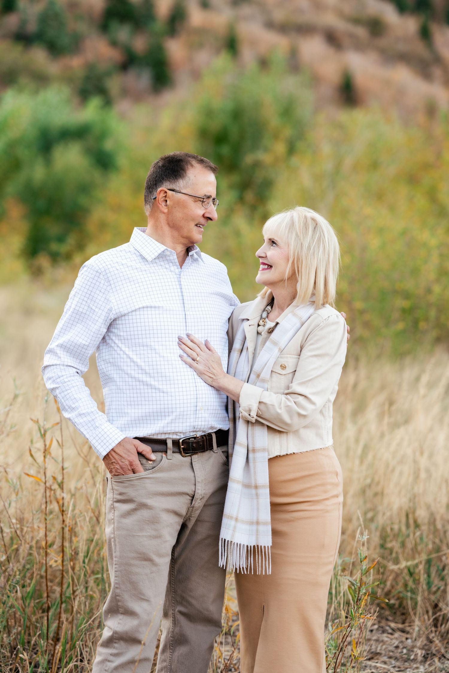 A mature couple shares a joyful moment together in a field with mountains behind them.