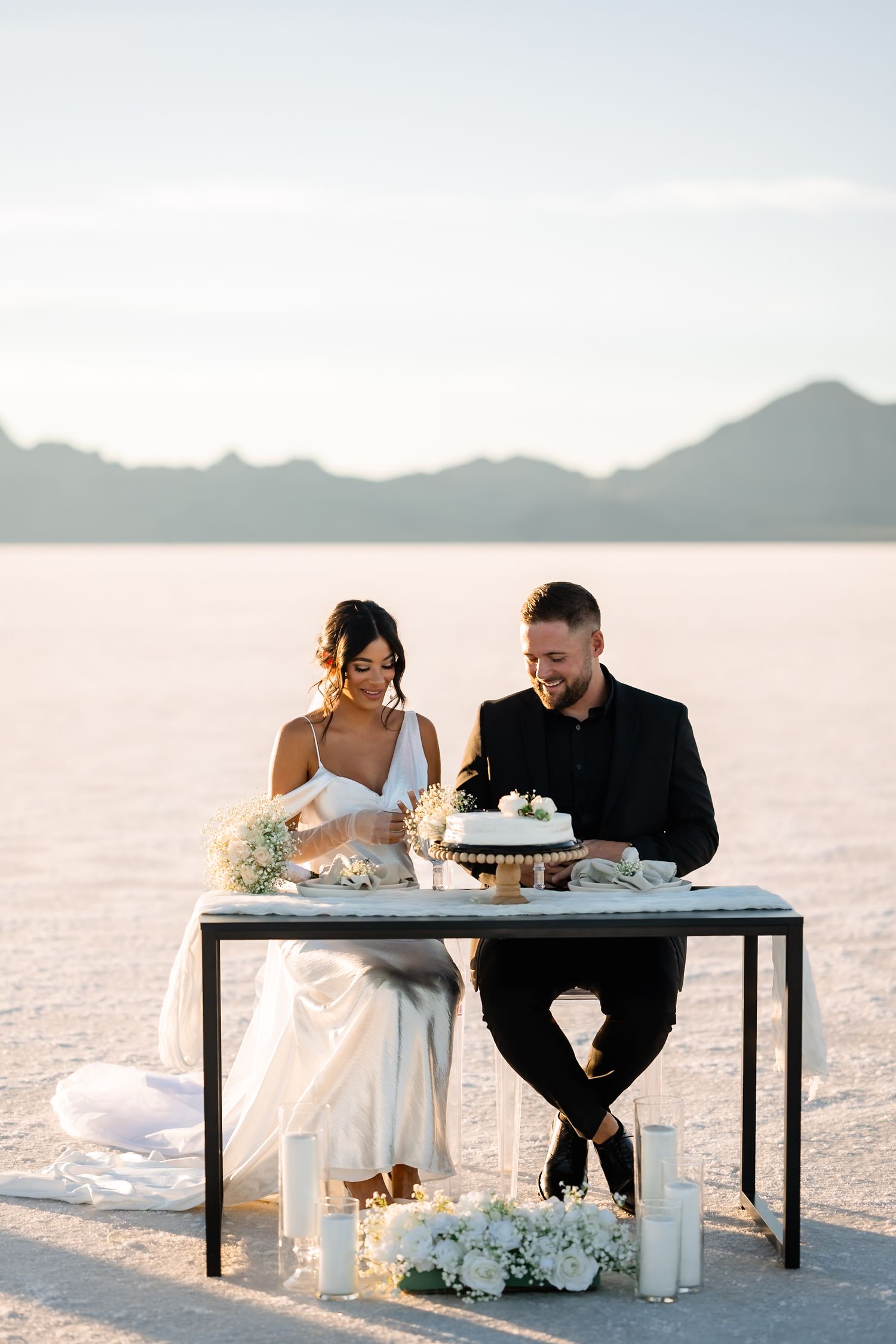 A newlywed couple shares a moment at a modern table setup on salt flats with mountains in the background.