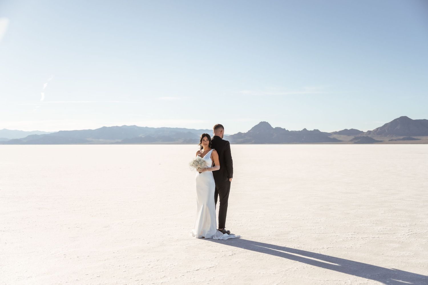 A wedding ceremony takes place on the stark white landscape of a salt flat with mountains in the background.