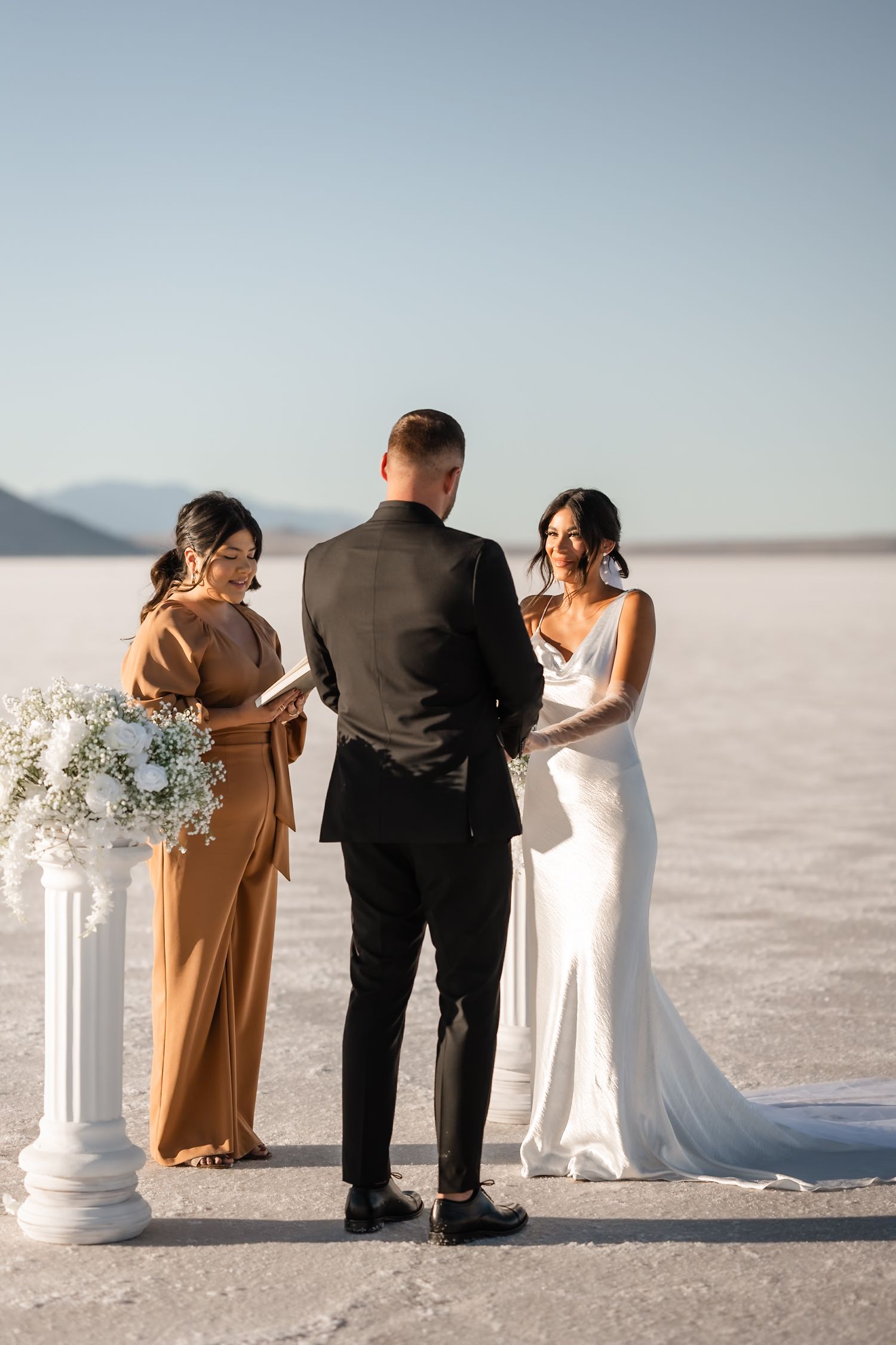 Intimate outdoor wedding ceremony on salt flats with white floral decorations.