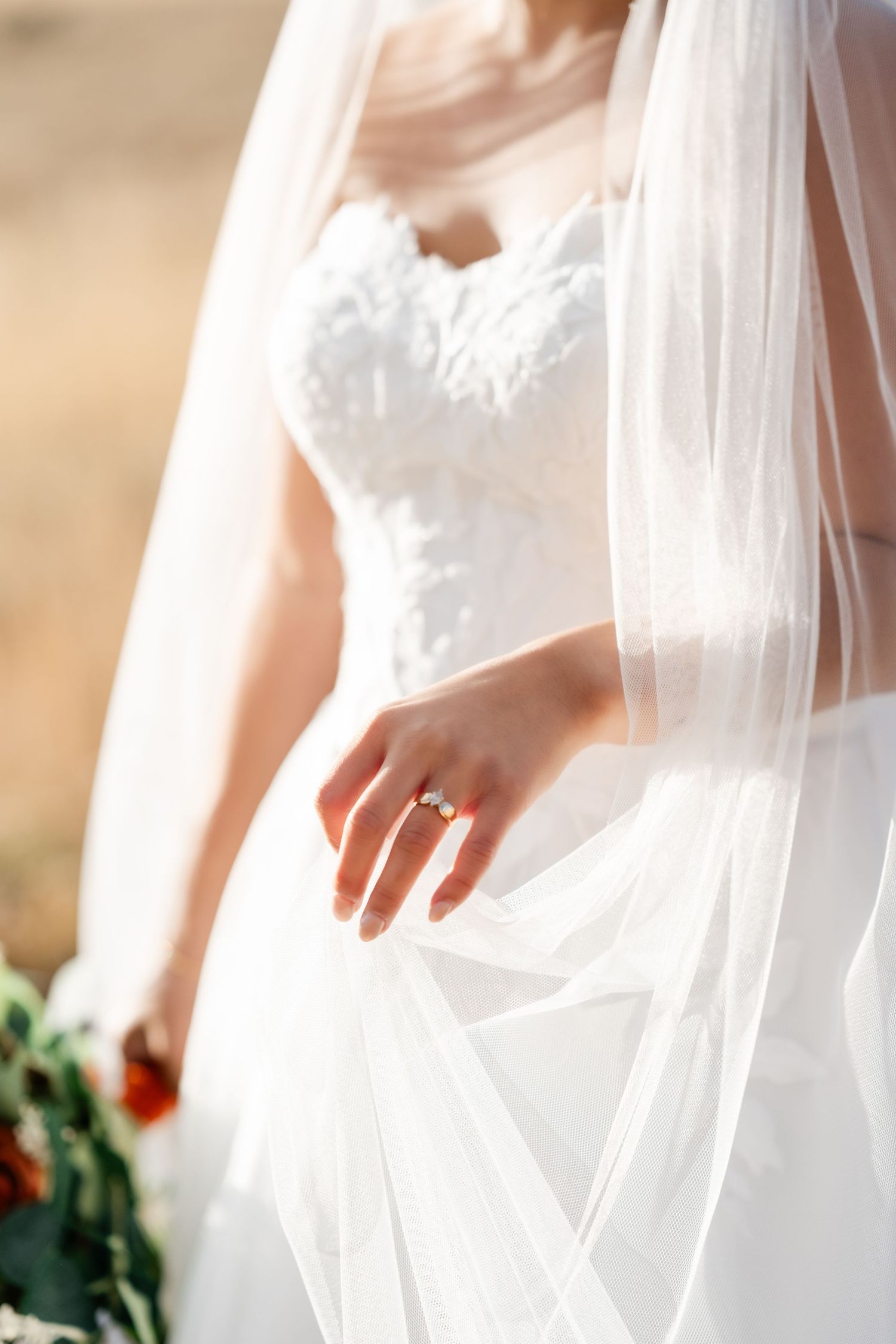 Close-up details of flowing white wedding dress veil against soft beige background.