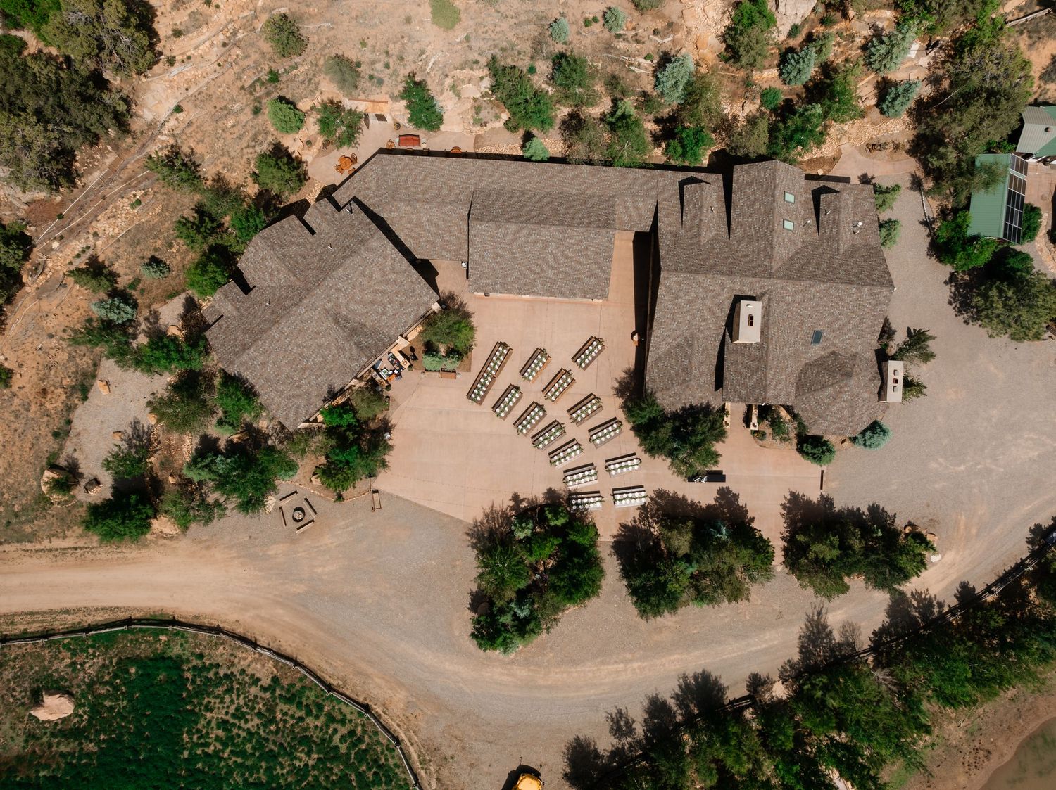 Aerial view of a winding dirt road leading through desert terrain with scattered trees and buildings.