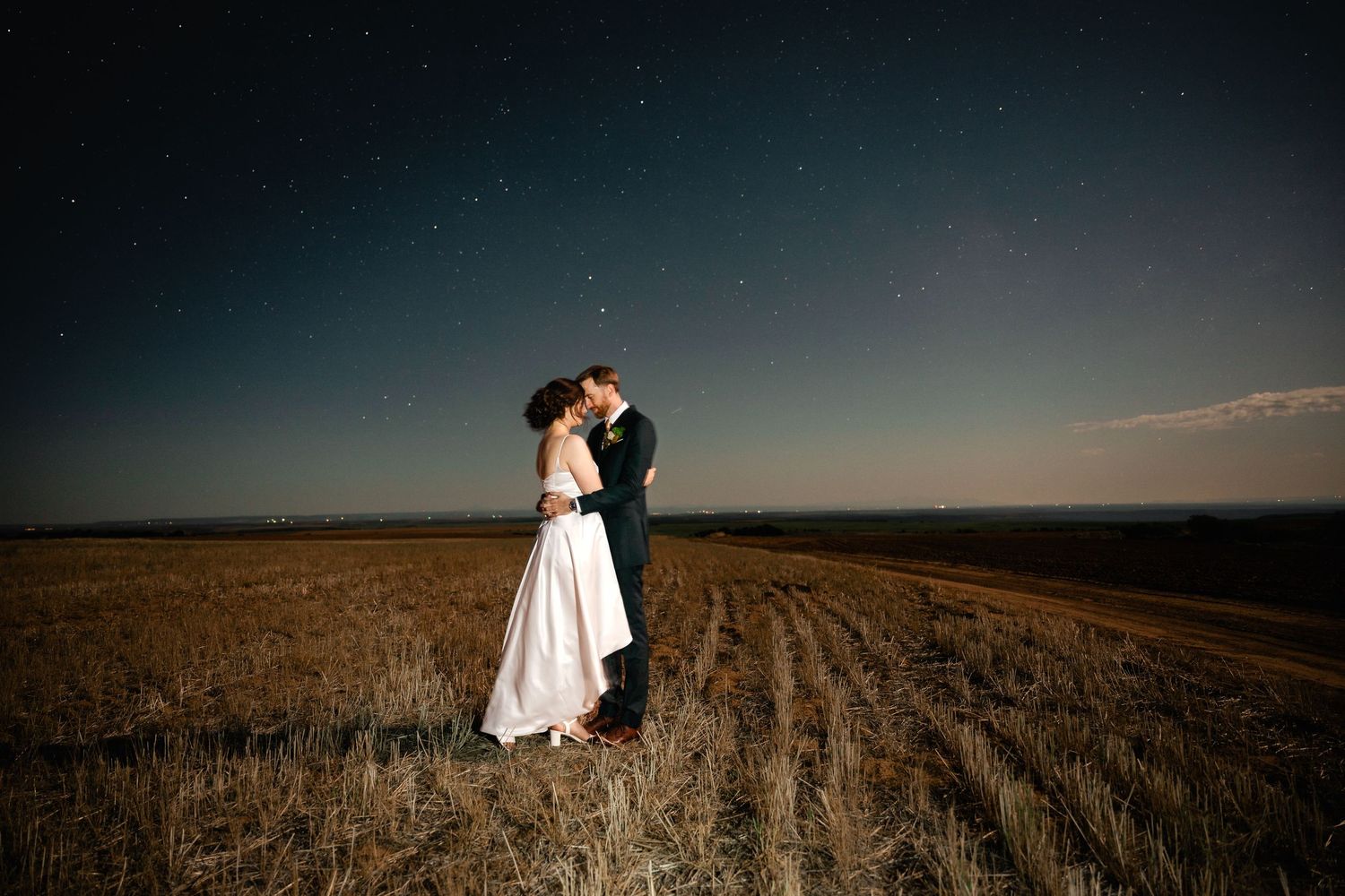 A romantic sunset wedding portrait silhouetted against a vast agricultural field.