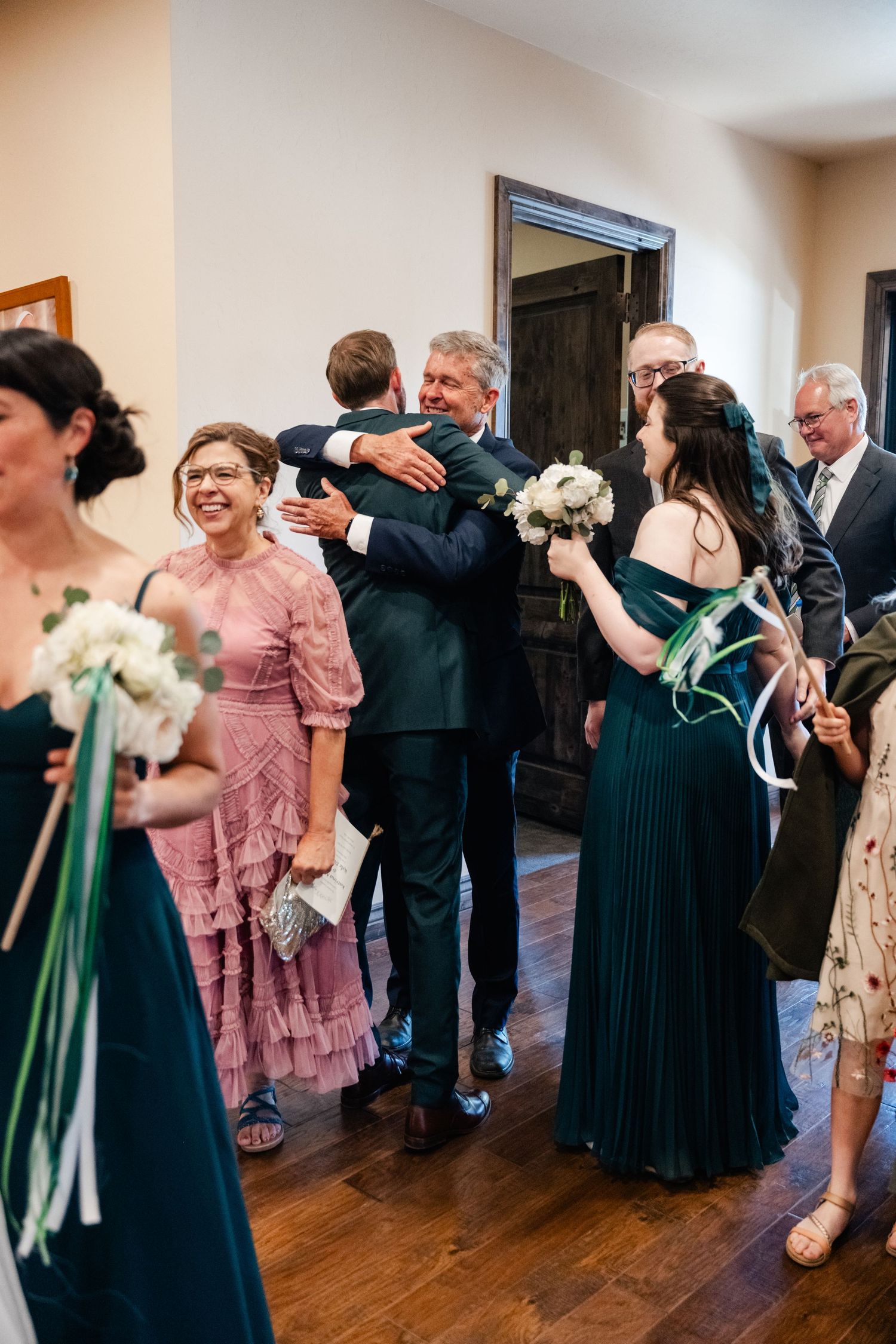 Wedding reception guests dance and celebrate in an indoor venue with hardwood floors and white walls.