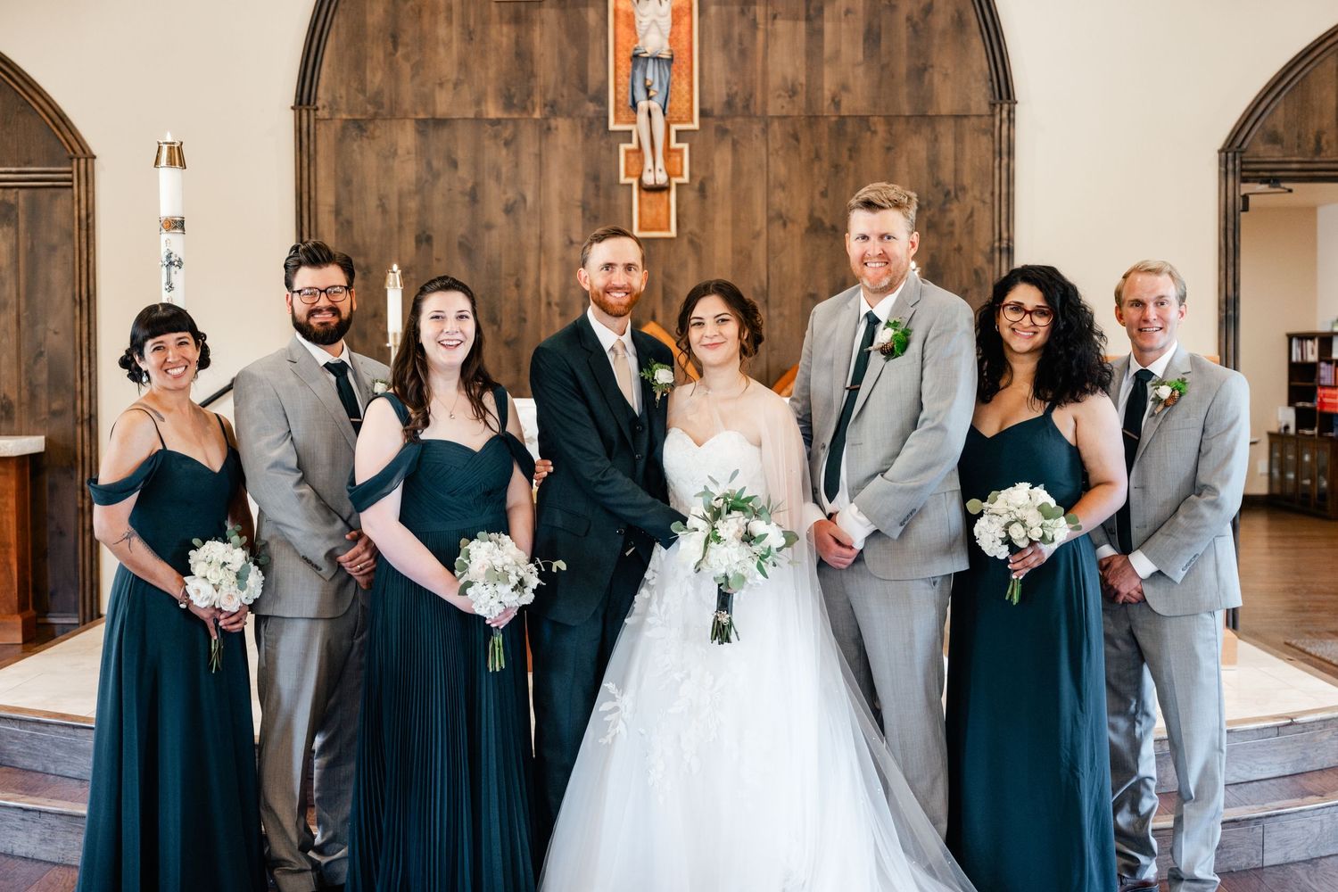 Wedding party in formal attire poses together in an elegant church hallway with arched architecture.